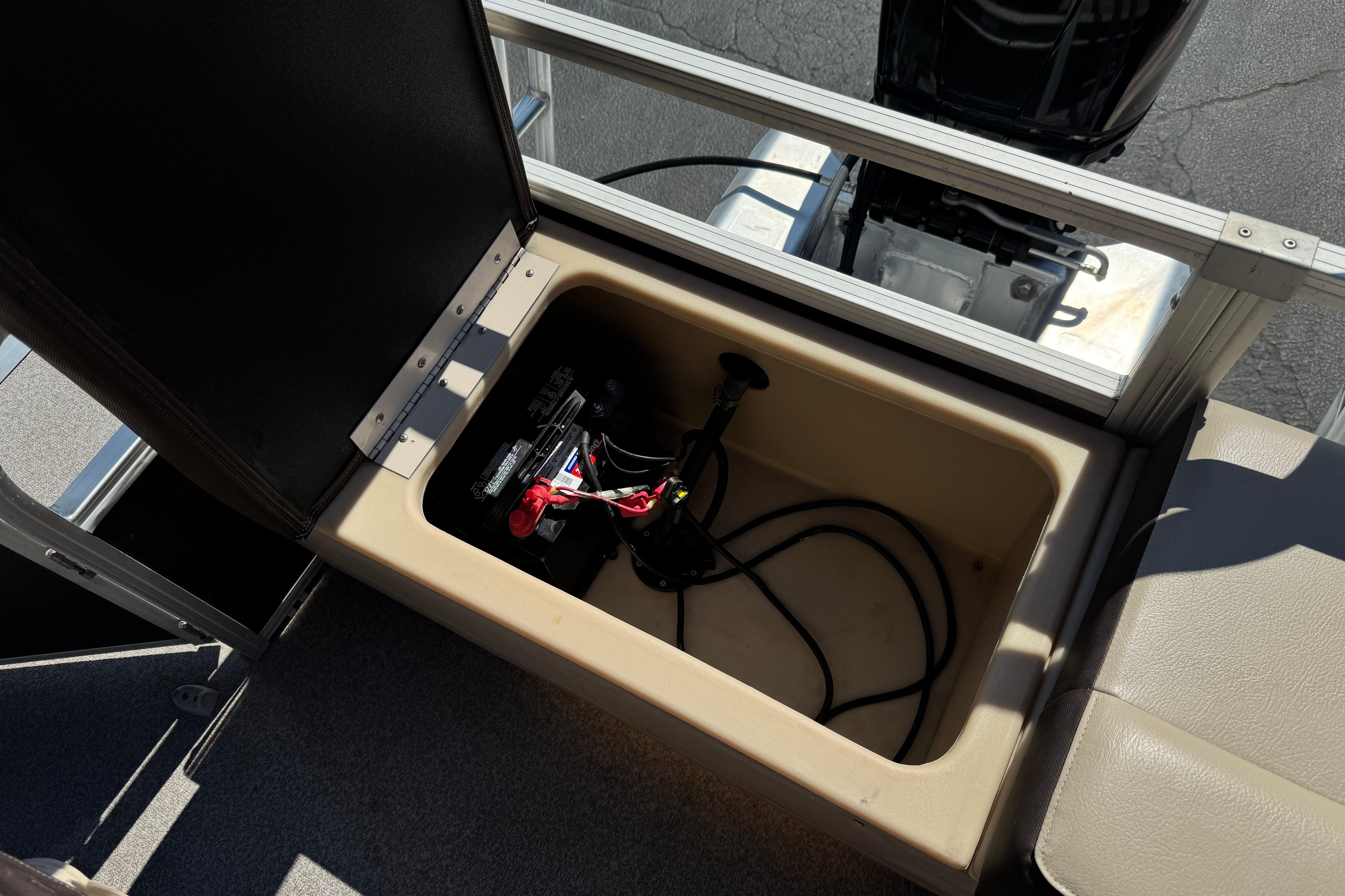 Open storage compartment on 2018 Sun Tracker SportFish 22 DLX boat, revealing battery and cables.