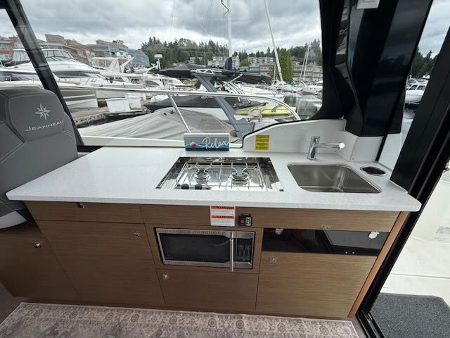 The 2021 Jeanneau NC 1095 galley features a stove, sink, and microwave.