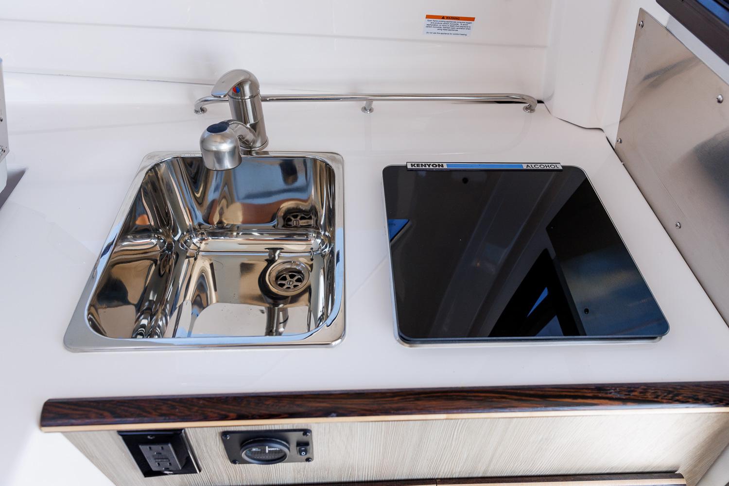 Compact kitchen area in Solara 250-C boat, featuring a stainless steel sink and electric cooktop.
