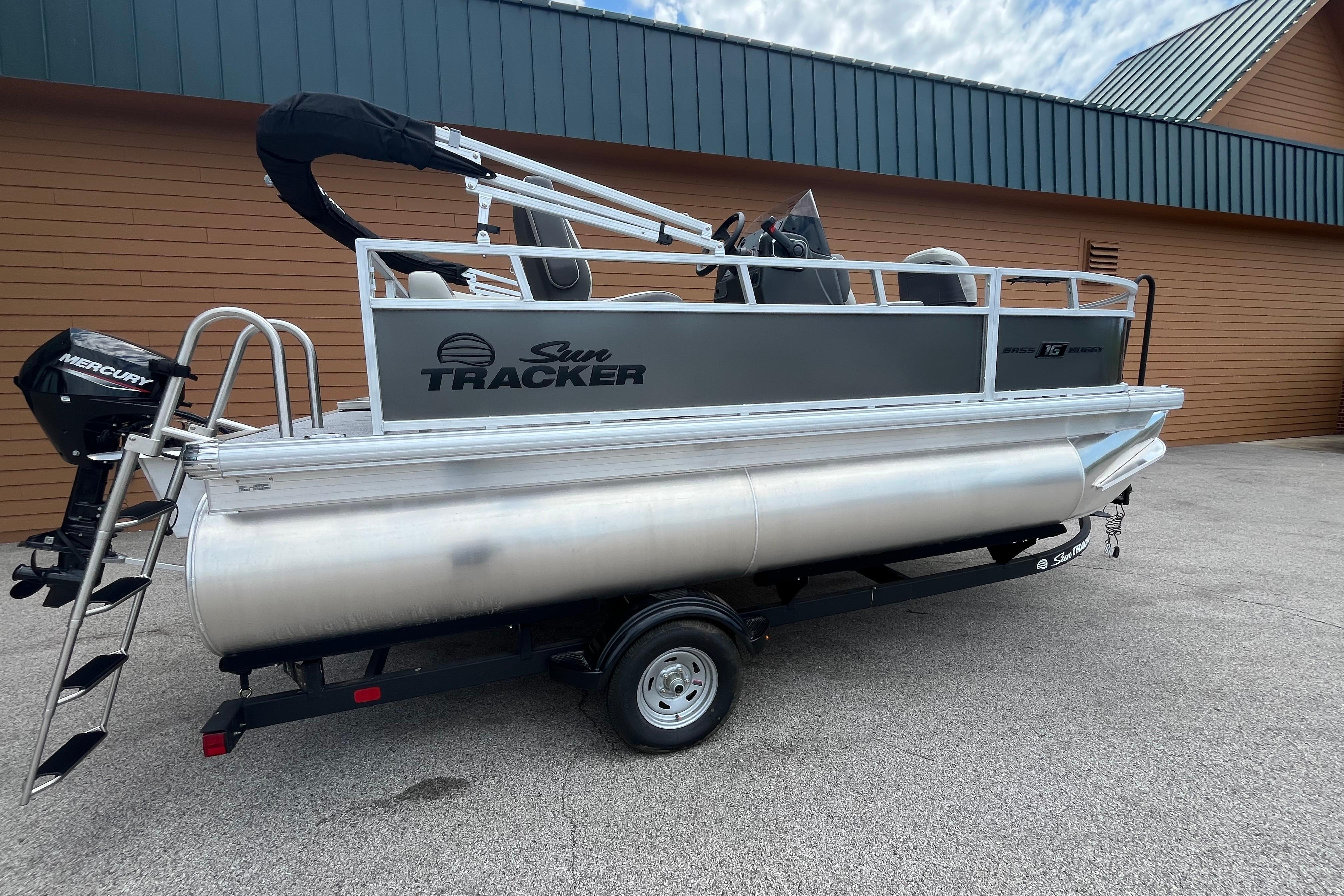 2026 Sun Tracker Bass Buggy 16 XL Select pontoon boat on trailer, parked outdoors.