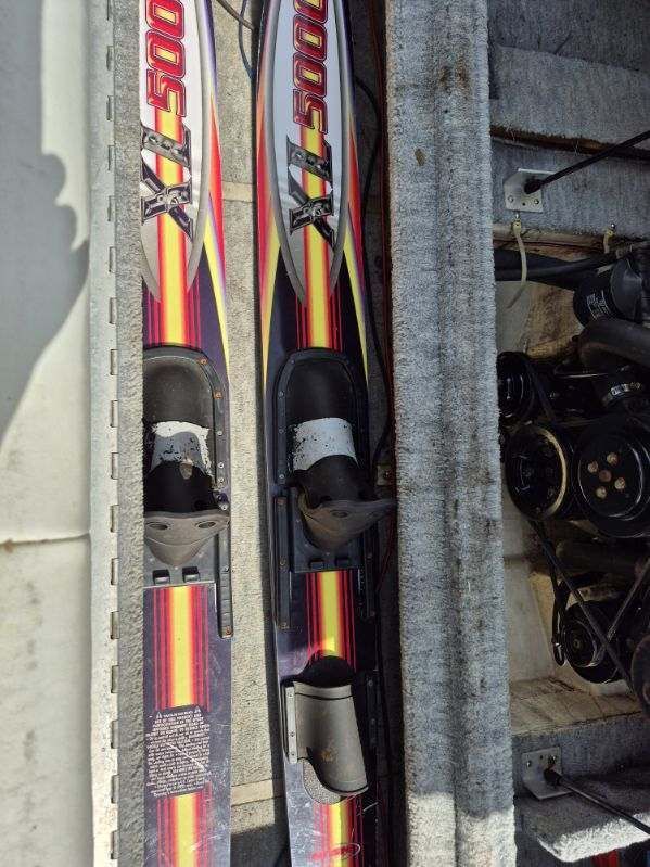 Two water skis are lying in a boat, surrounded by gray carpeting.