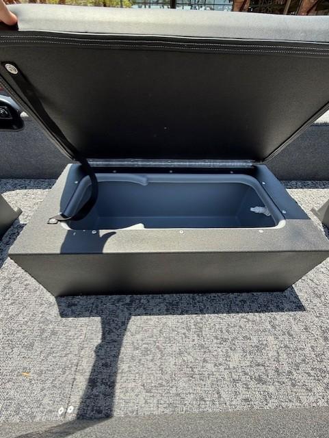 Open storage compartment in 2025 Tracker Panfish 17 boat, featuring gray interior and carpeted flooring.