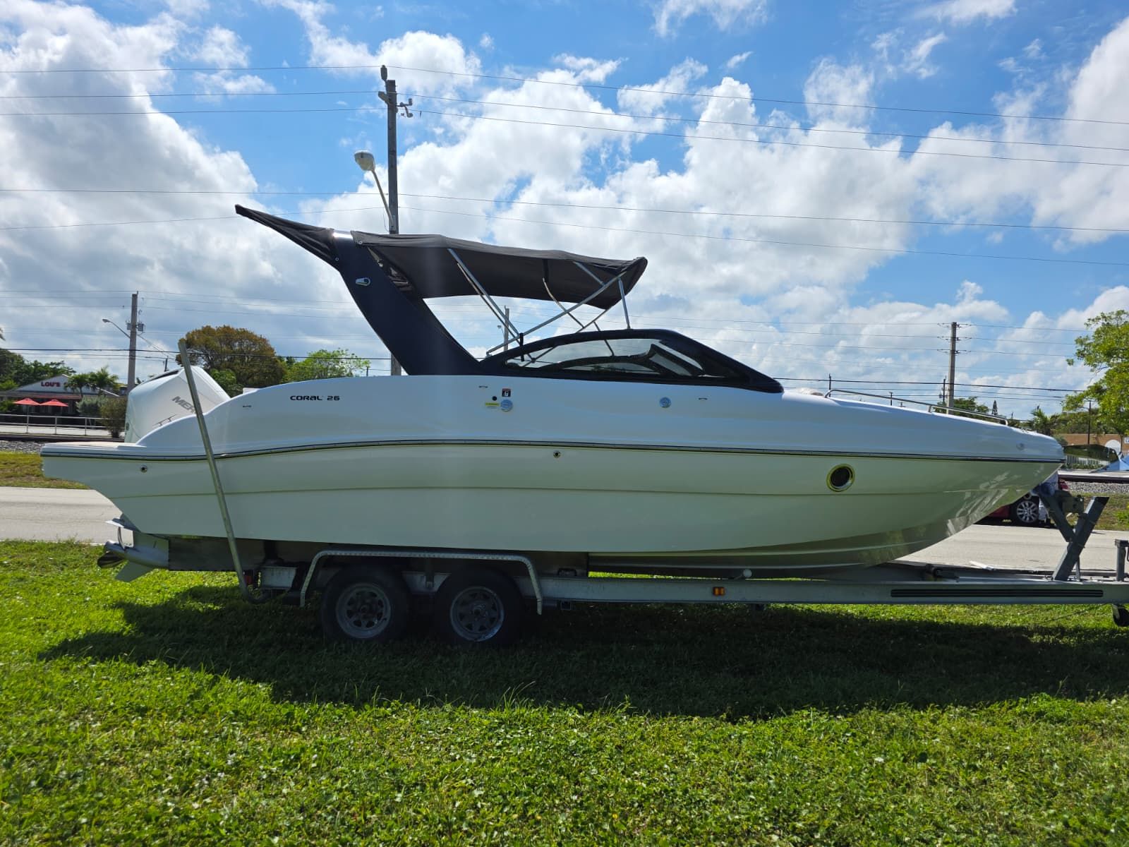 A 2025 Coral 26 boat on a trailer, set on a grassy area.