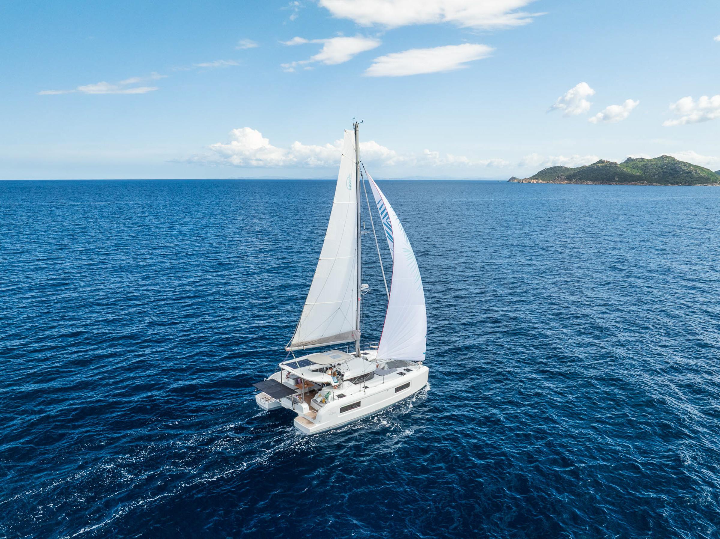 2025 Lagoon 38 catamaran sailing on open sea near a distant island.