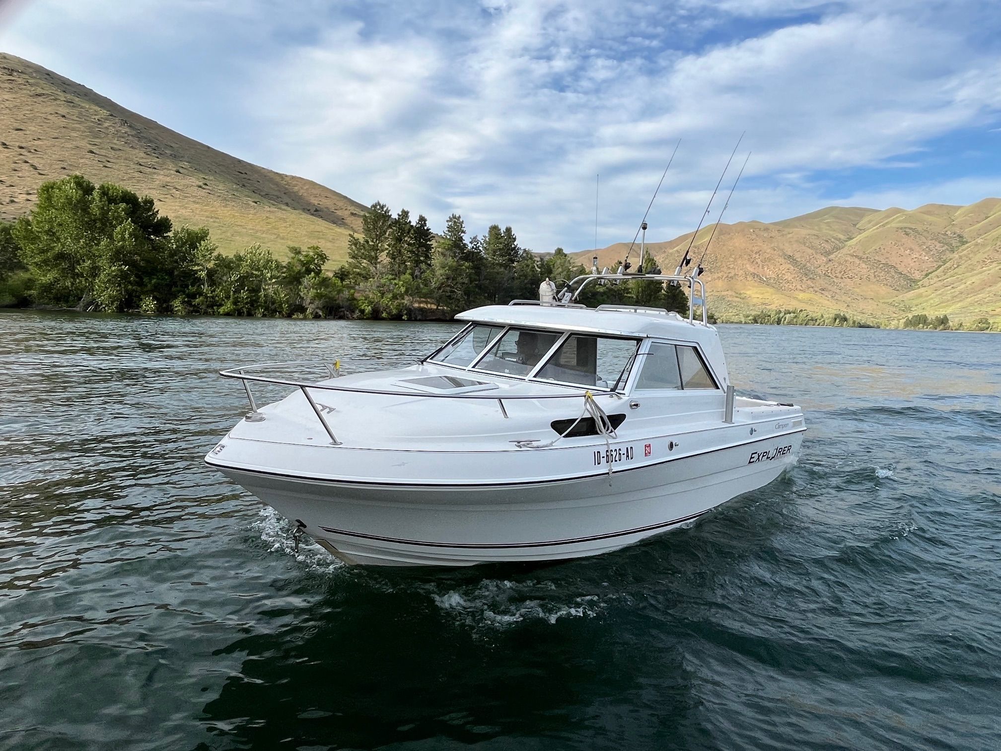 A white boat cruising on a calm lake, surrounded by green hills.