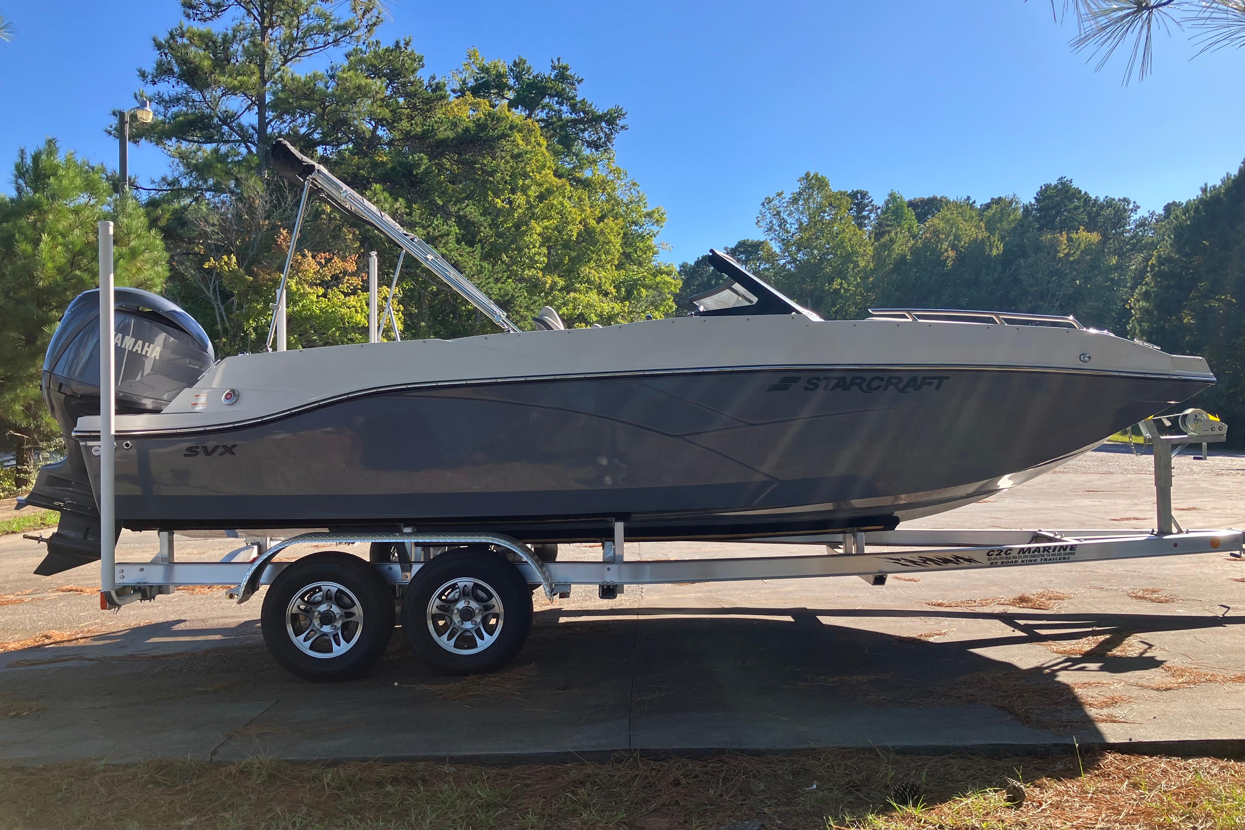 2025 Starcraft SVX 210 OB boat on trailer, parked outdoors, surrounded by trees.
