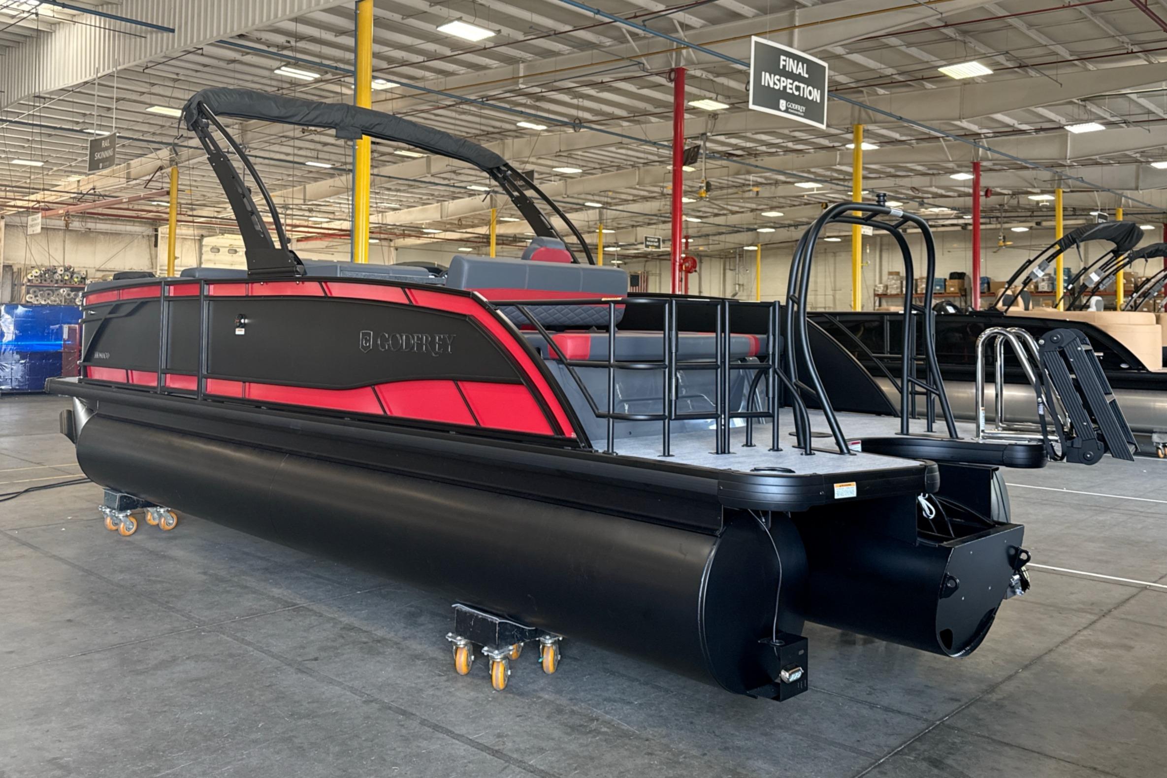 2027 Godfrey Monaco 25' Tritoon in warehouse, featuring sleek black and red design.