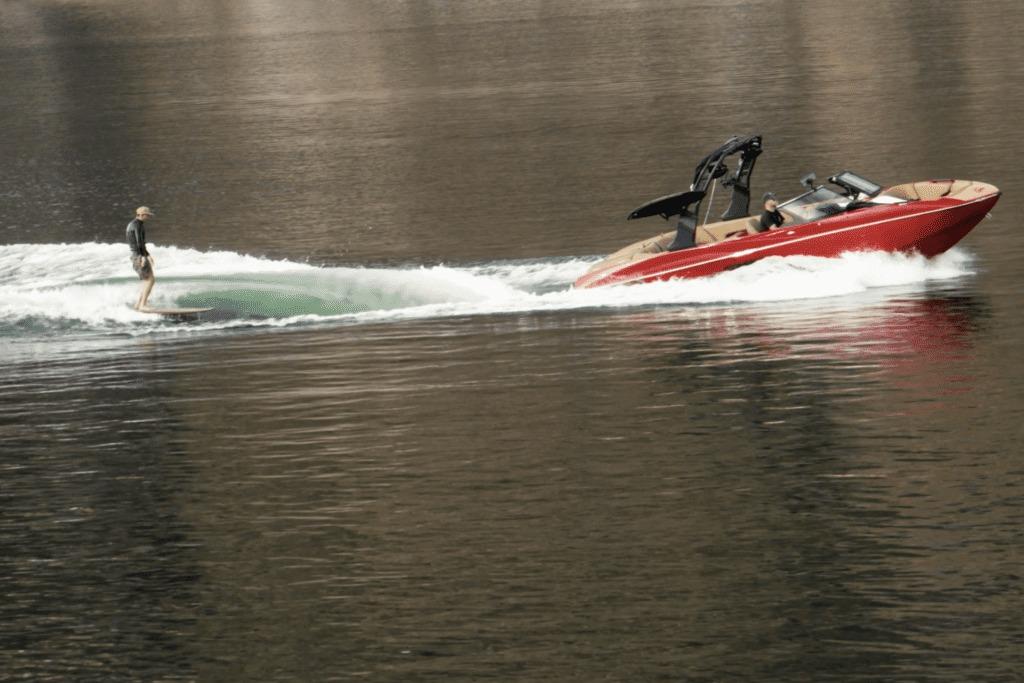 Wakeboarder riding behind a 2027 MB B52 23 Classic boat on a calm lake.