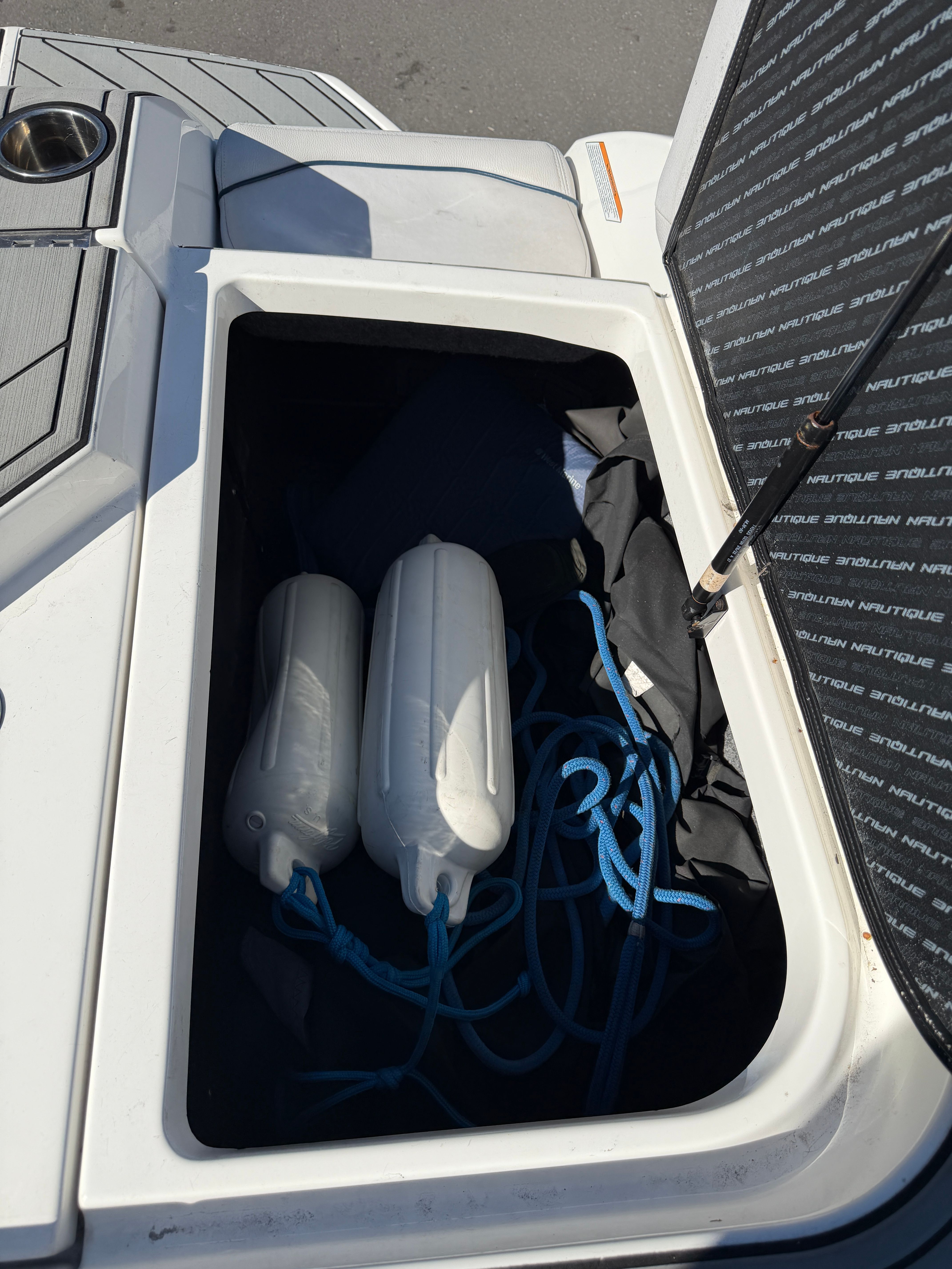 An open storage compartment on a boat with two fenders and blue ropes.