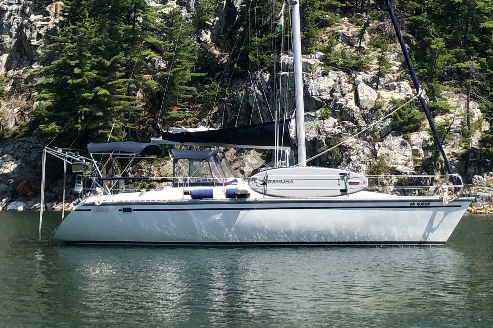 1989 Hunter Legend 37 sailboat anchored near rocky shoreline with trees.