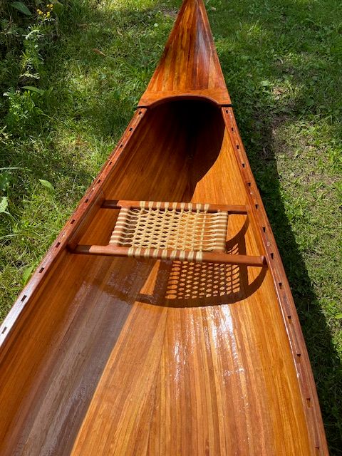 A handcrafted cedar strip canoe with a woven seat on green grass.