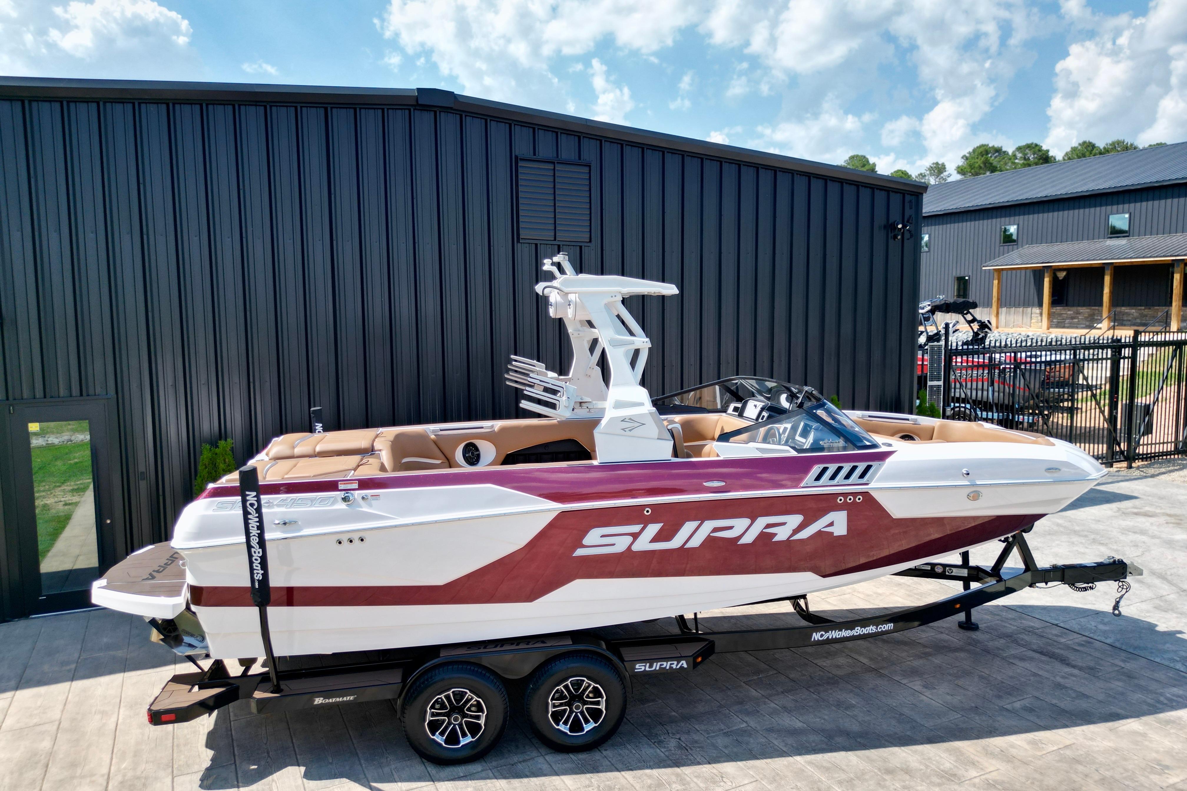 2021 Supra SE boat on trailer, parked outside a modern building under a blue sky.