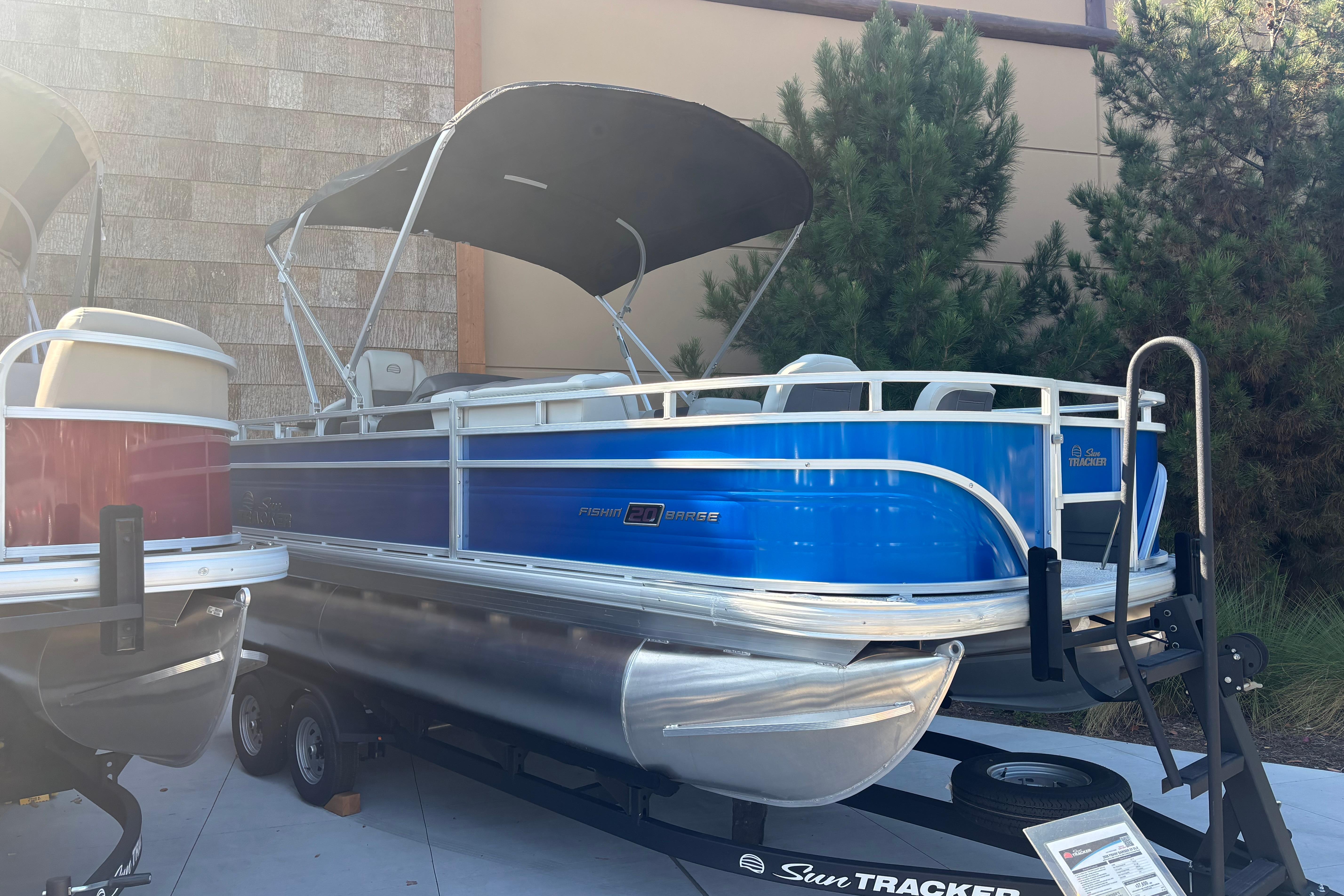 2026 Sun Tracker Fishin' Barge 20 DLX pontoon boat with blue exterior on trailer.