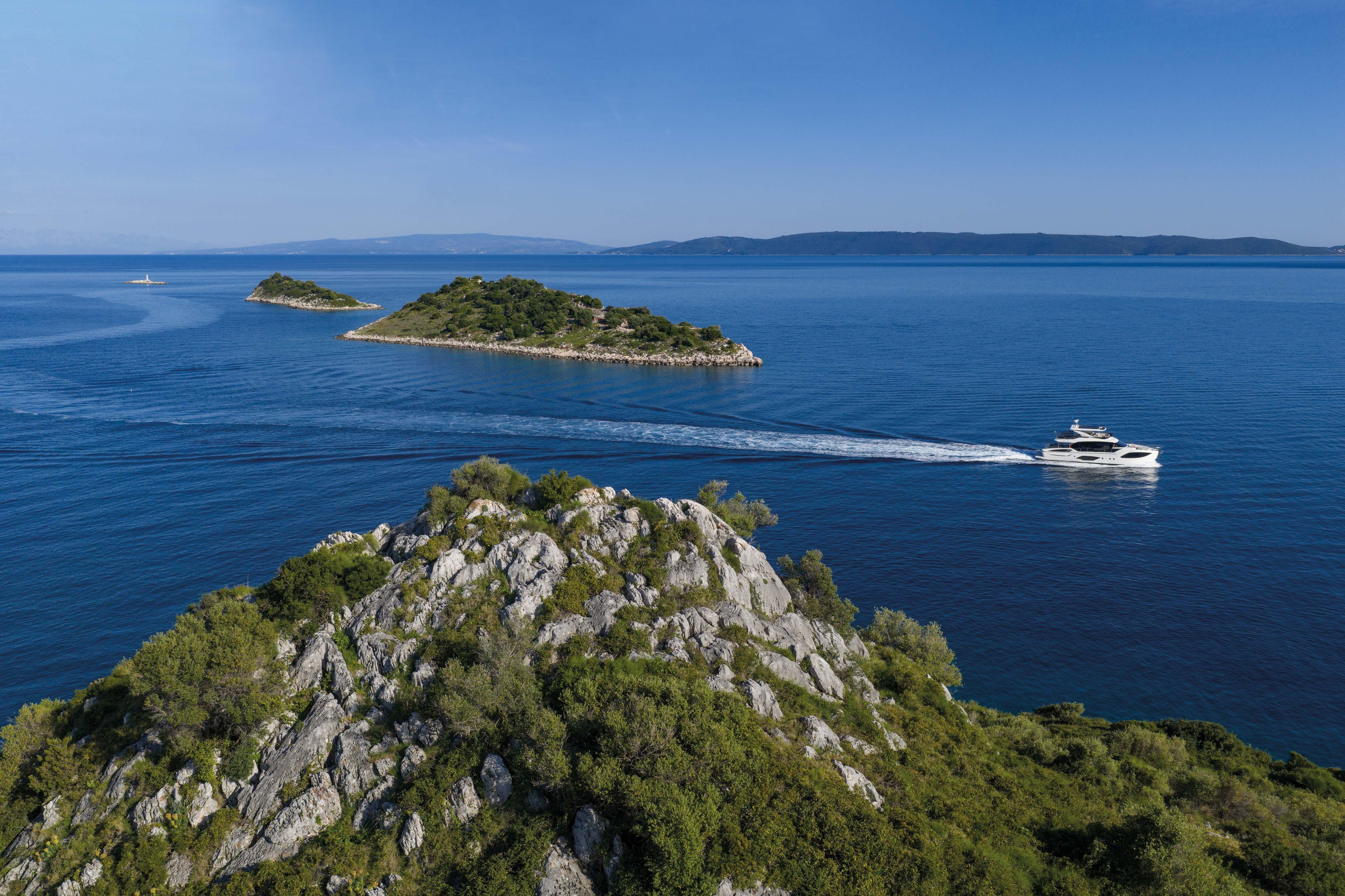 A luxury yacht cruises on calm waters, surrounded by small green islands.