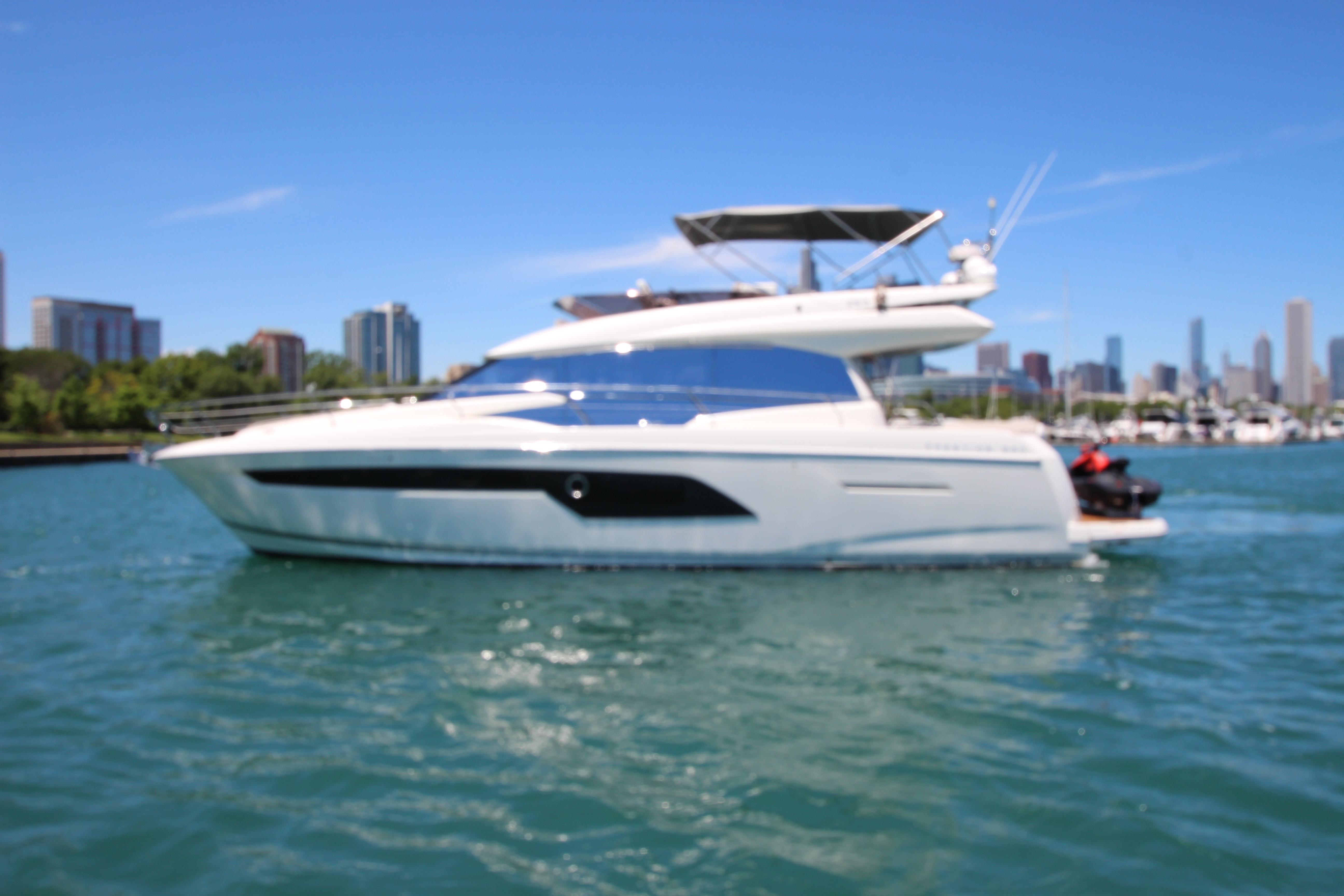 Luxurious 2022 Prestige 520 yacht cruising on a sunny day with city skyline backdrop.