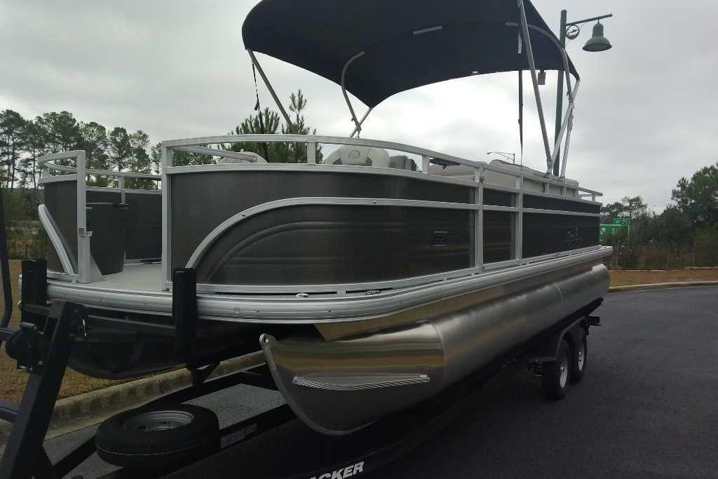 2026 Sun Tracker Fishin' Barge 22 DLX pontoon boat on trailer, parked outdoors.