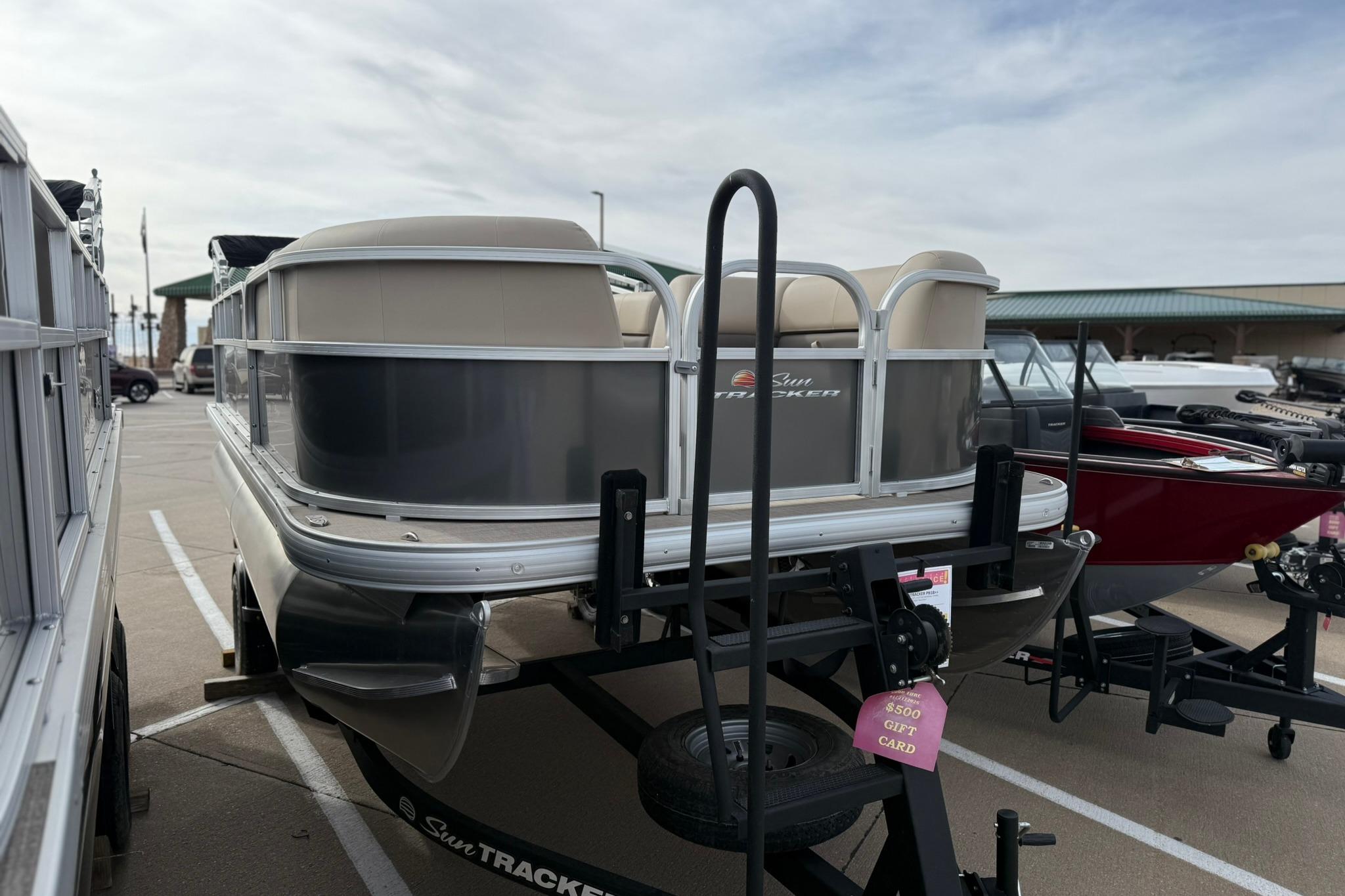 2025 Sun Tracker Party Barge 18 DLX pontoon boat on trailer in parking lot.