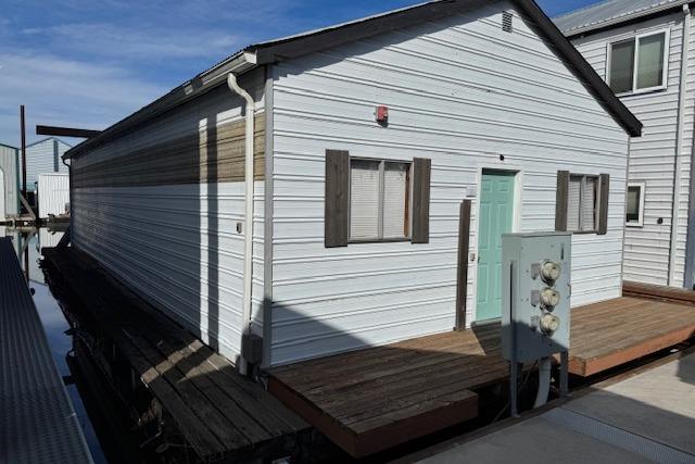 1960 custom boathouse with white siding and teal door, docked on a sunny day.