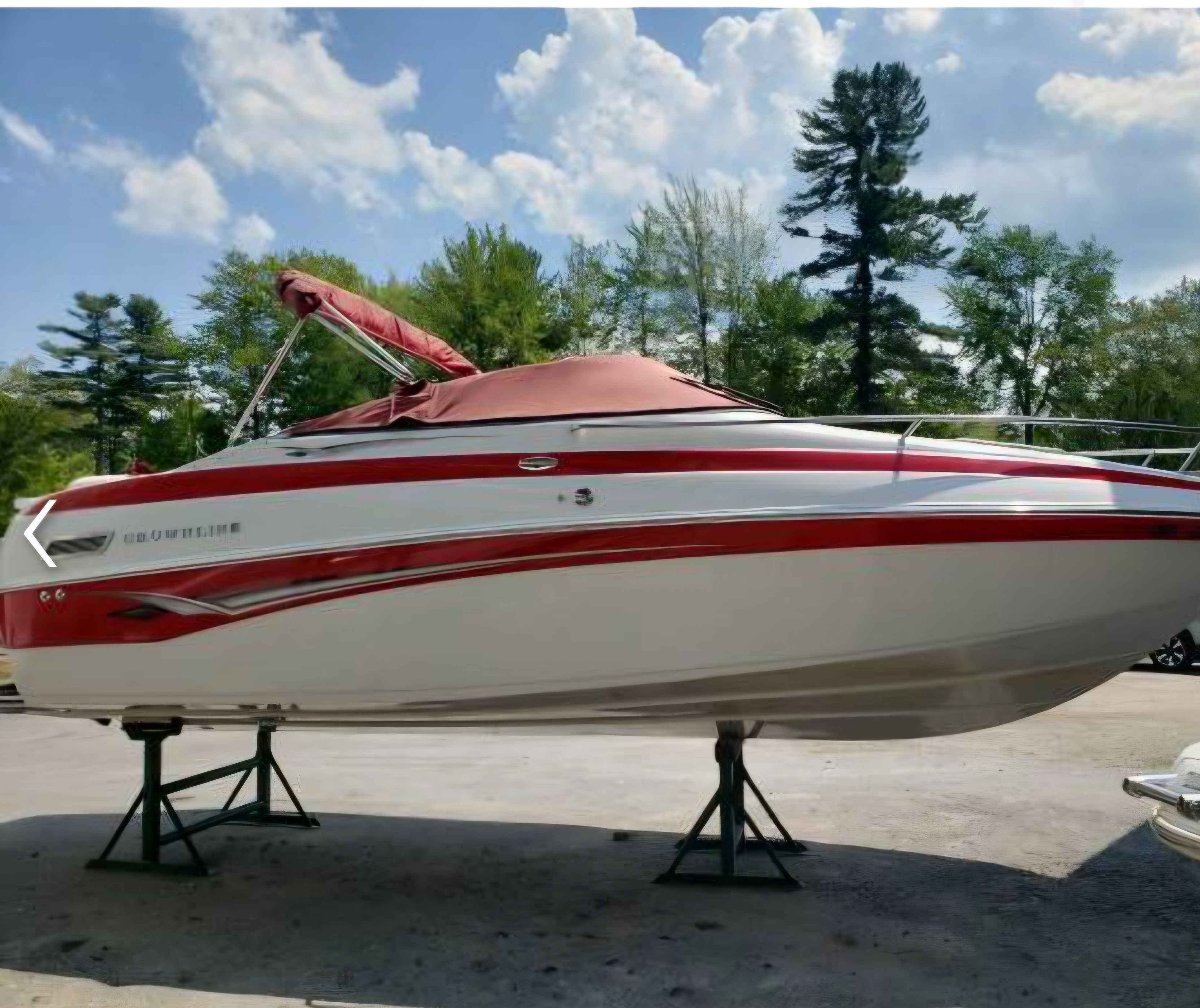 2003 Crownline 215CCR boat on stands, red canopy, sunny day.