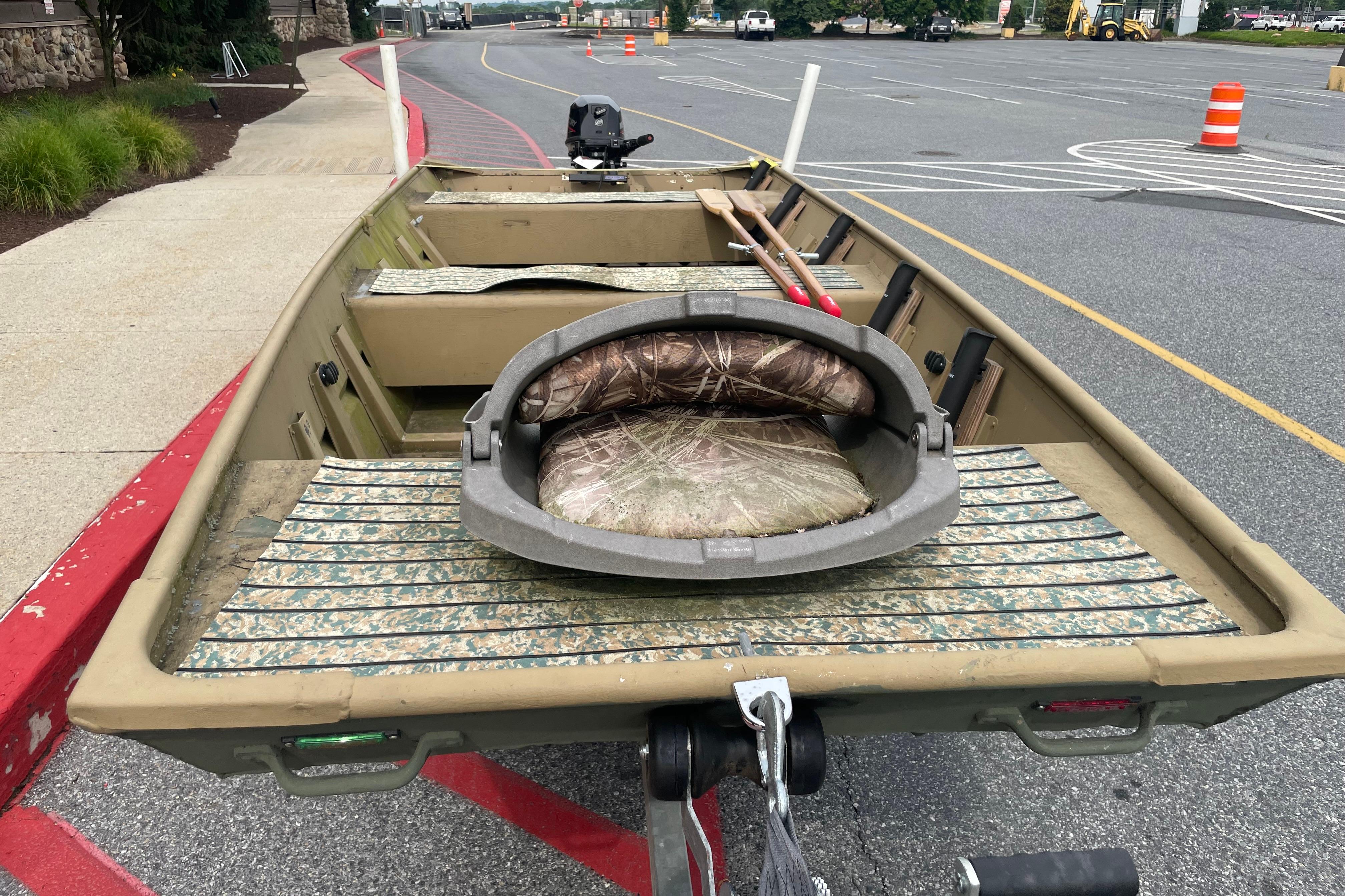 1986 Landau 1664 Jon boat with camouflage seating, parked on asphalt near traffic cones.