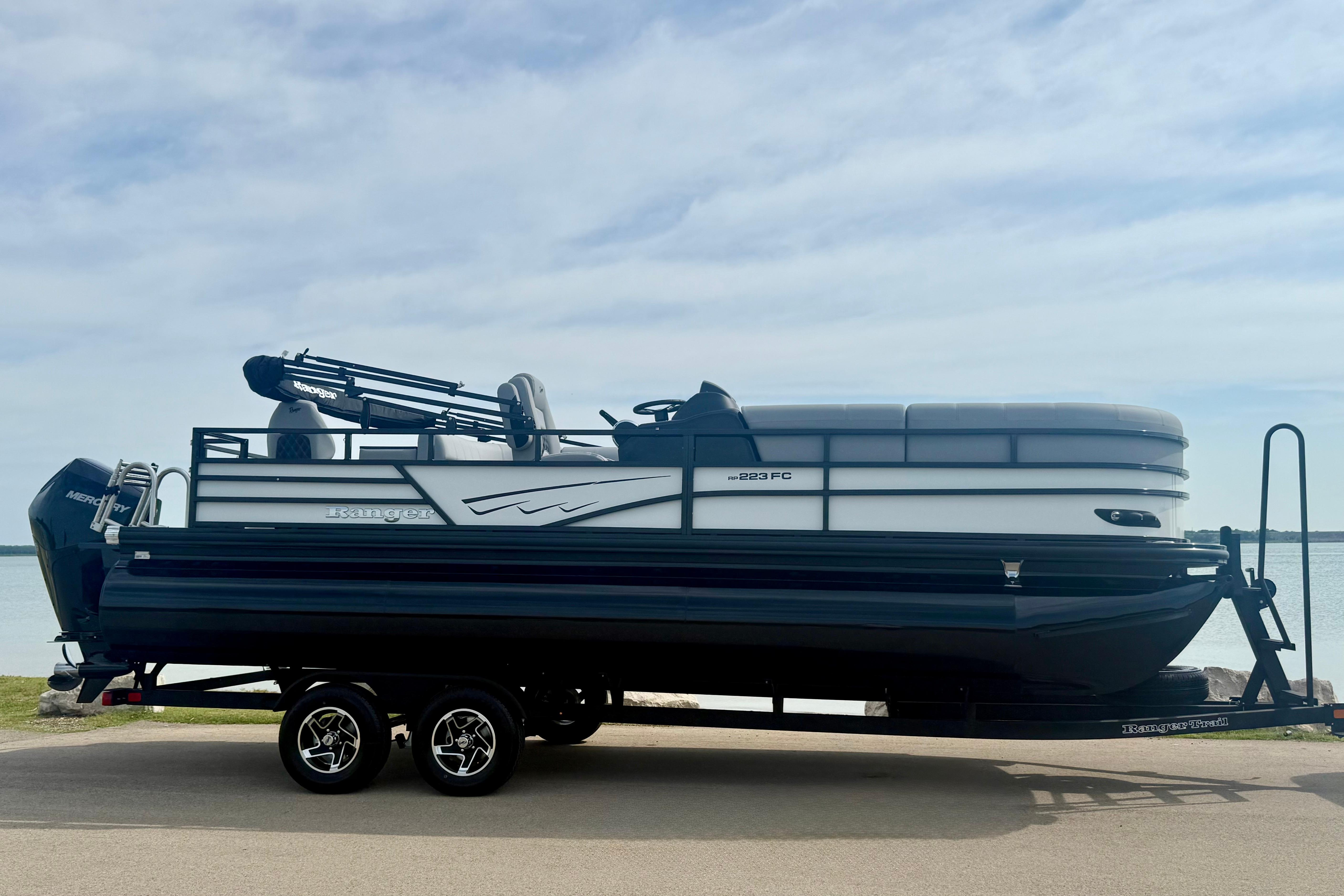 2026 Ranger 223FC pontoon boat on trailer by the water, under a cloudy sky.