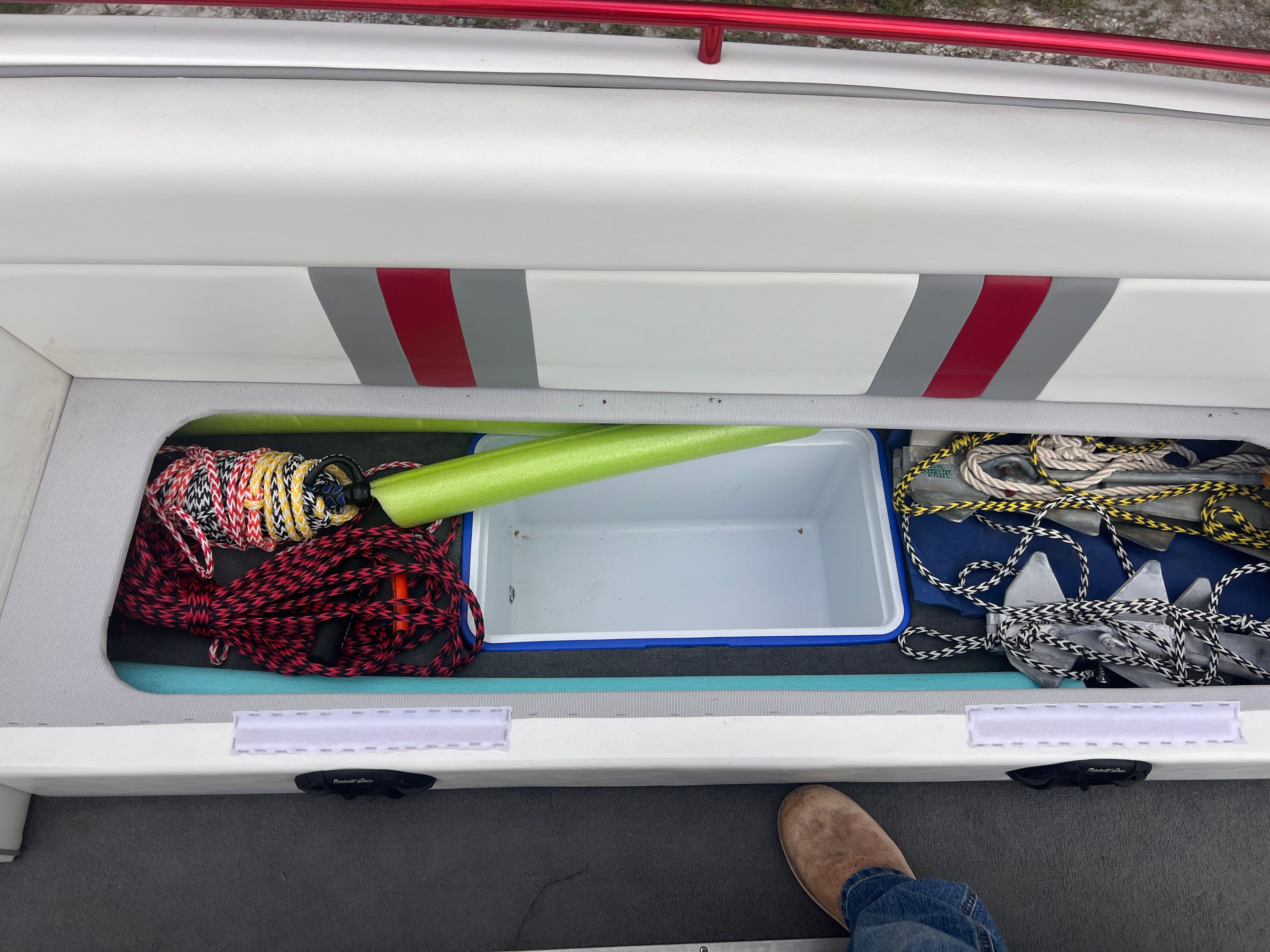 An open storage compartment on a boat with ropes and a green cone.