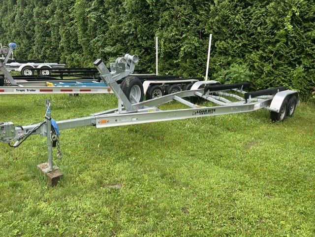 Boat trailer on green grass, surrounded by trees.