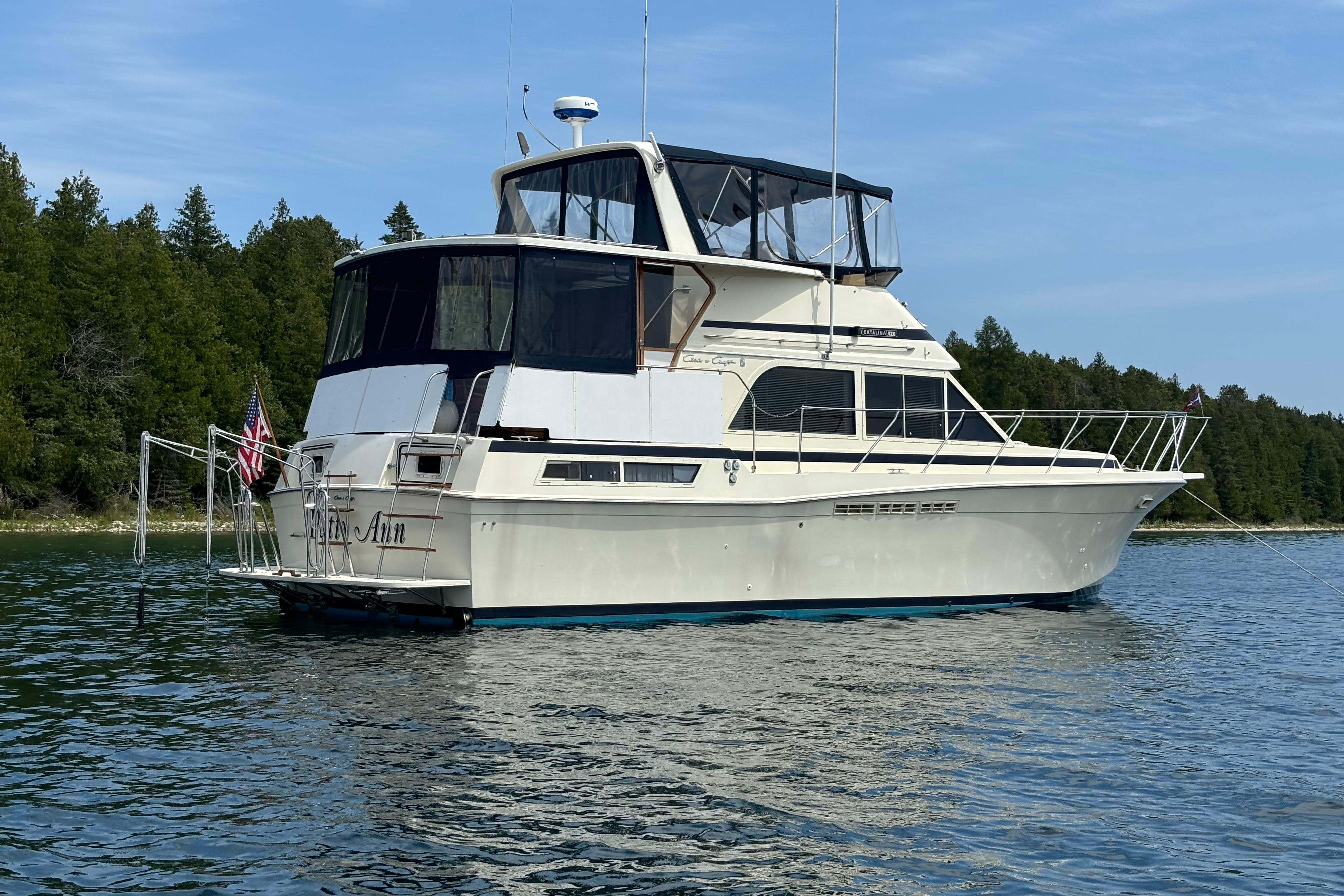 1987 Chris-Craft 427 Catalina yacht anchored on a serene lake with forested shoreline.