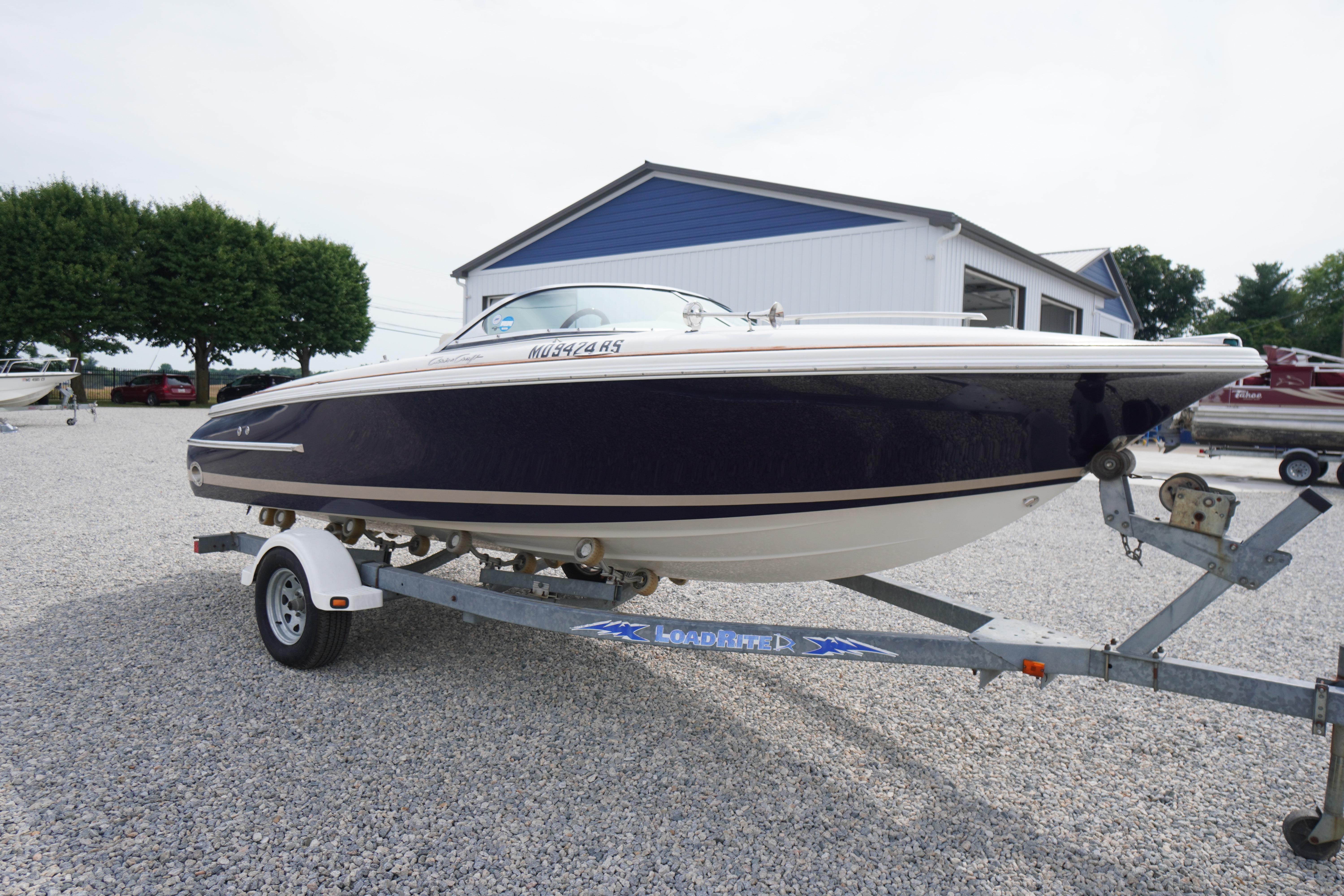 2005 Chris Craft Speedster Heritage boat on trailer in gravel lot.