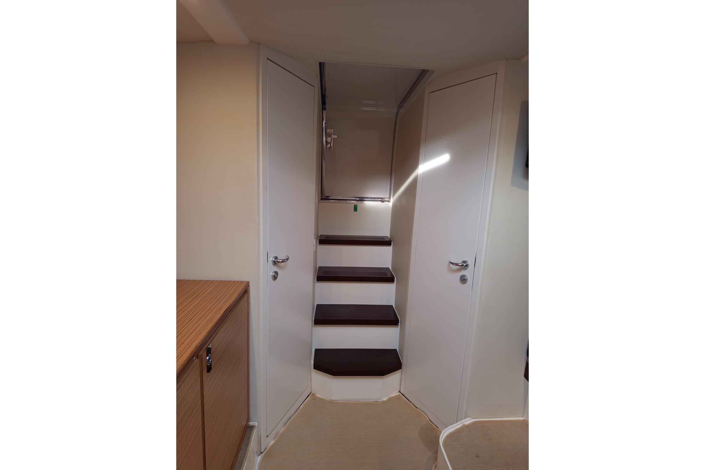 Interior stairs of 2008 Itama 40 yacht, featuring sleek wooden steps and white walls.