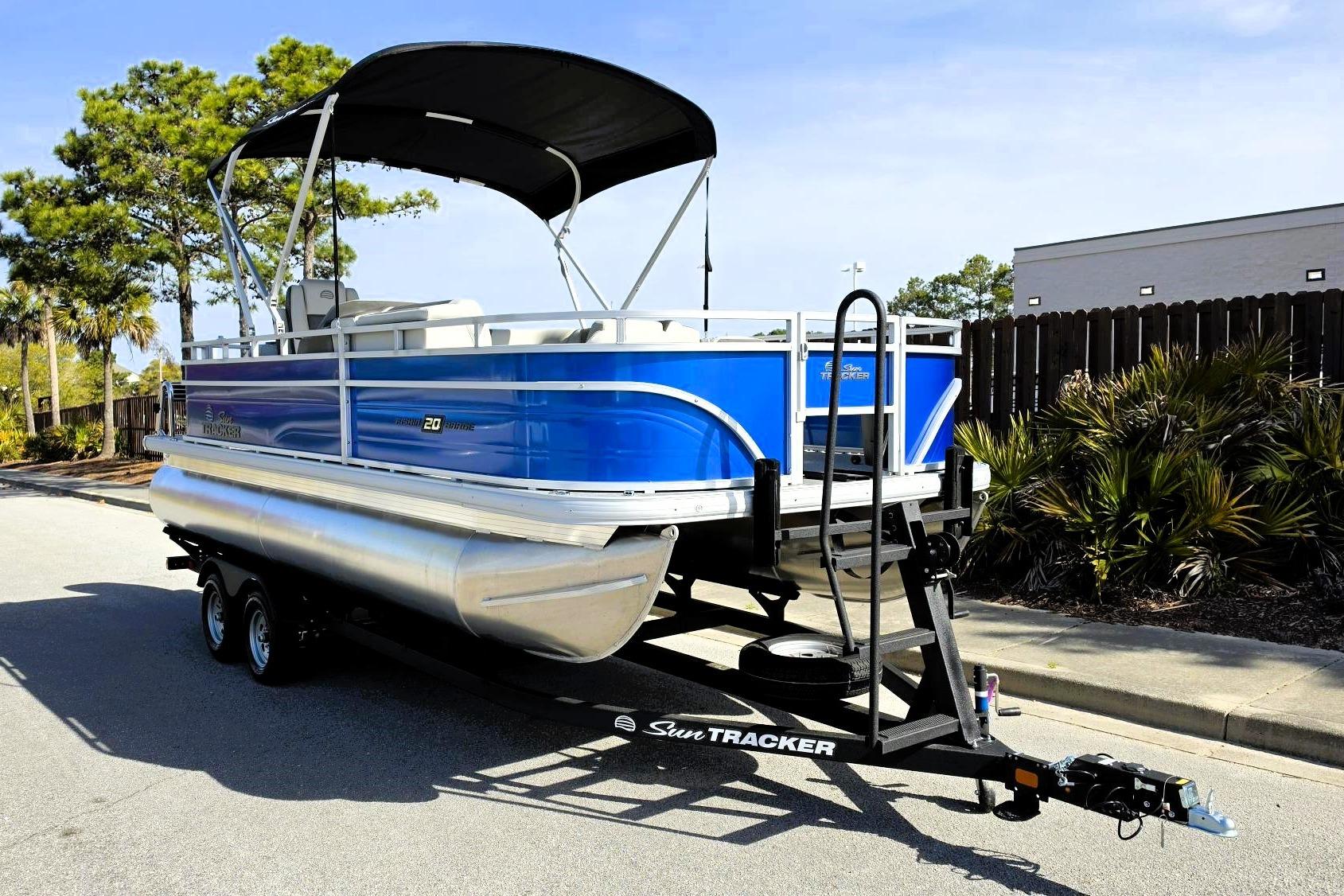 2026 Sun Tracker Fishin' Barge 20 DLX pontoon boat on trailer, parked outdoors.