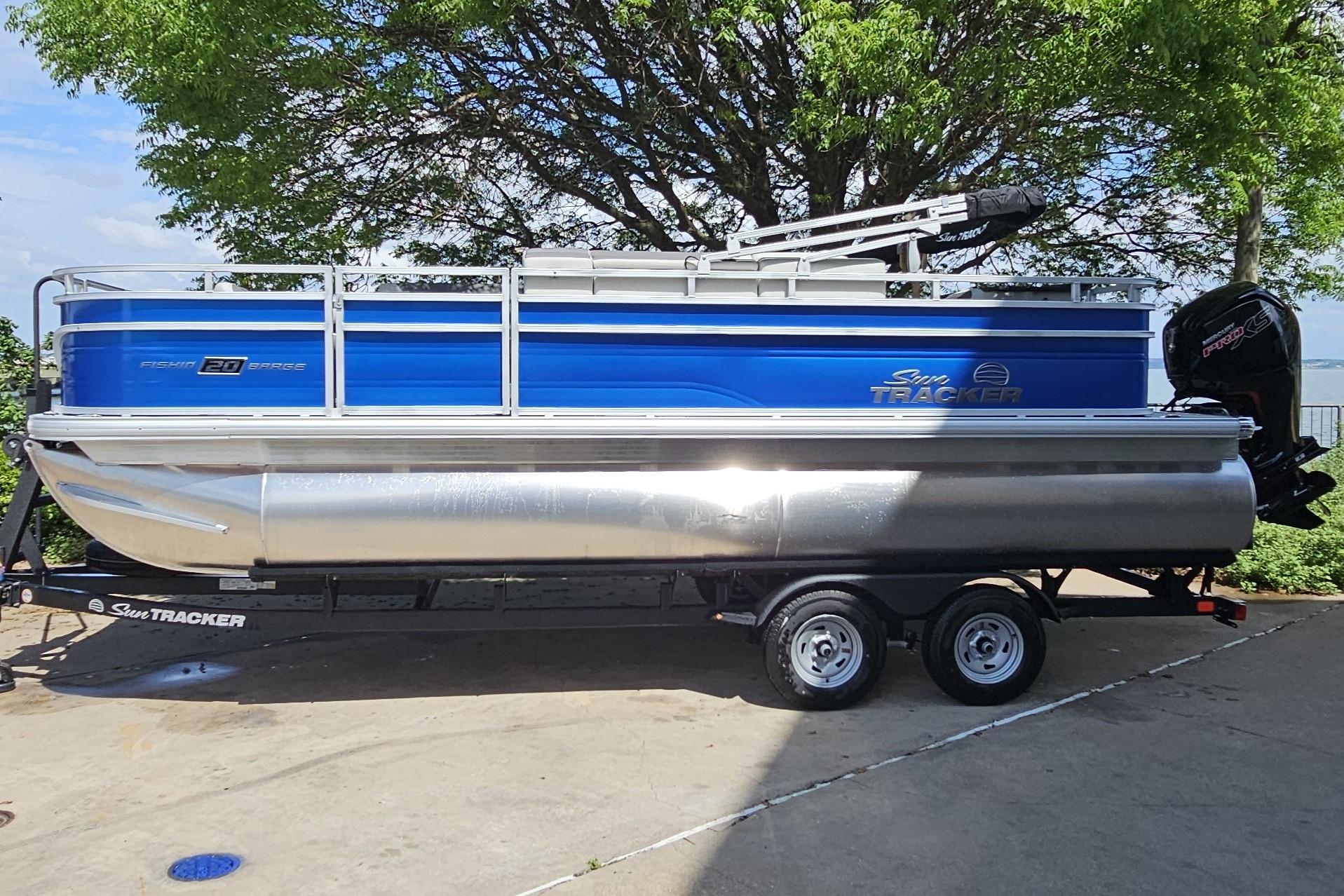 2026 Sun Tracker Fishin' Barge 20 DLX pontoon boat on trailer, parked outdoors.