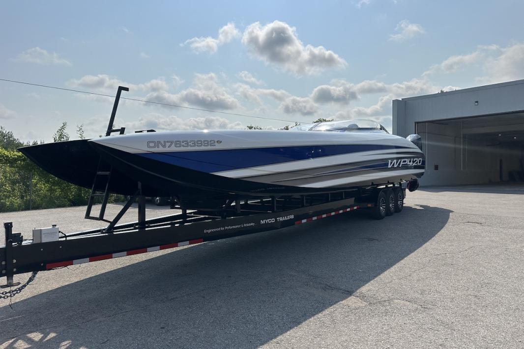 2018 Wright Performance 420 boat on trailer, parked outside a garage under a cloudy sky.