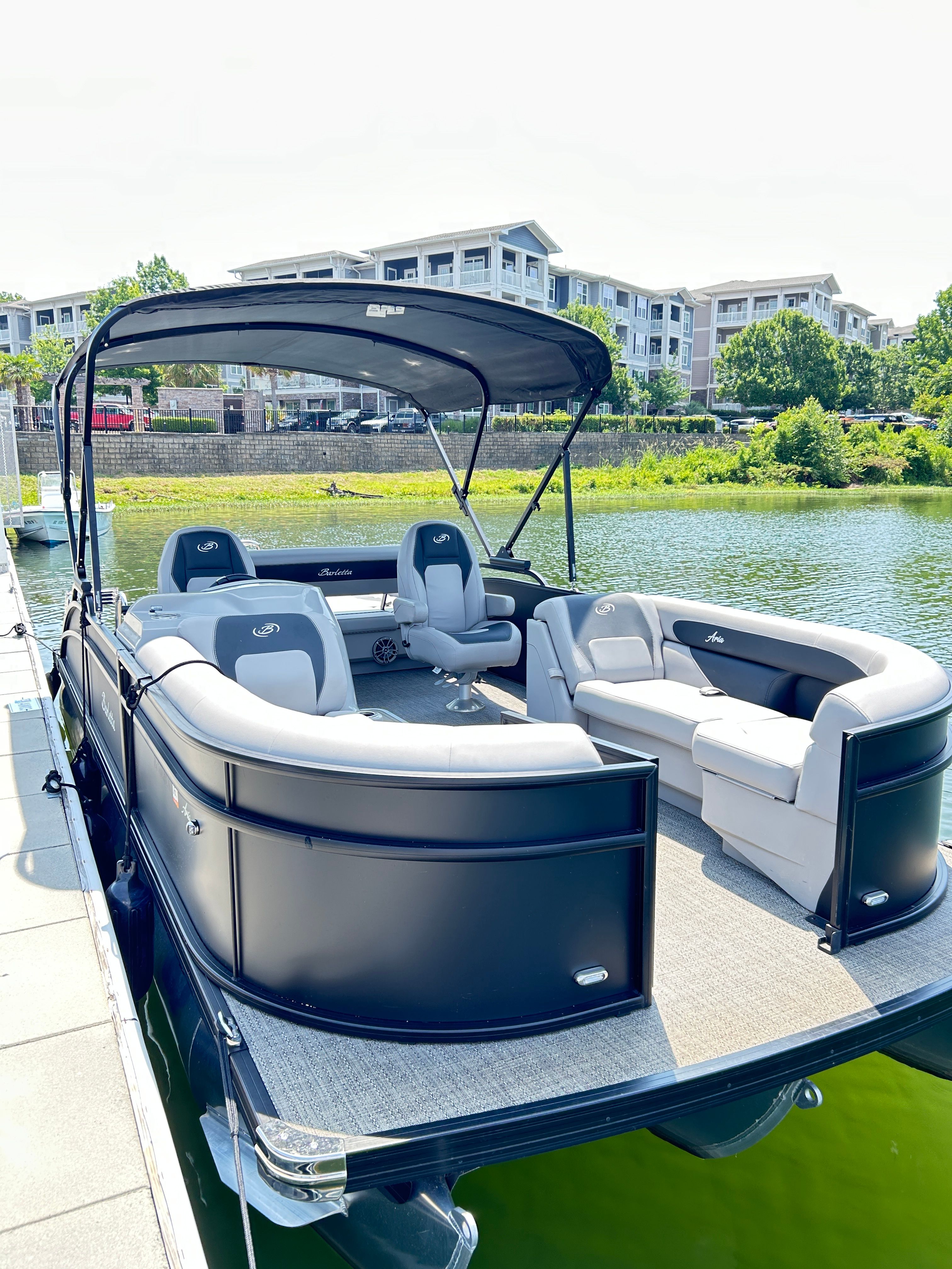A sleek pontoon boat with gray and black seating, docked on a sunny day.
