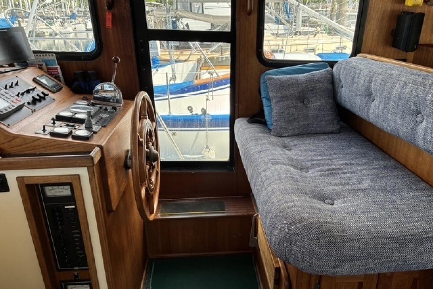 Cozy interior of a 2000 Nordic Tug 37 with helm and cushioned seating.