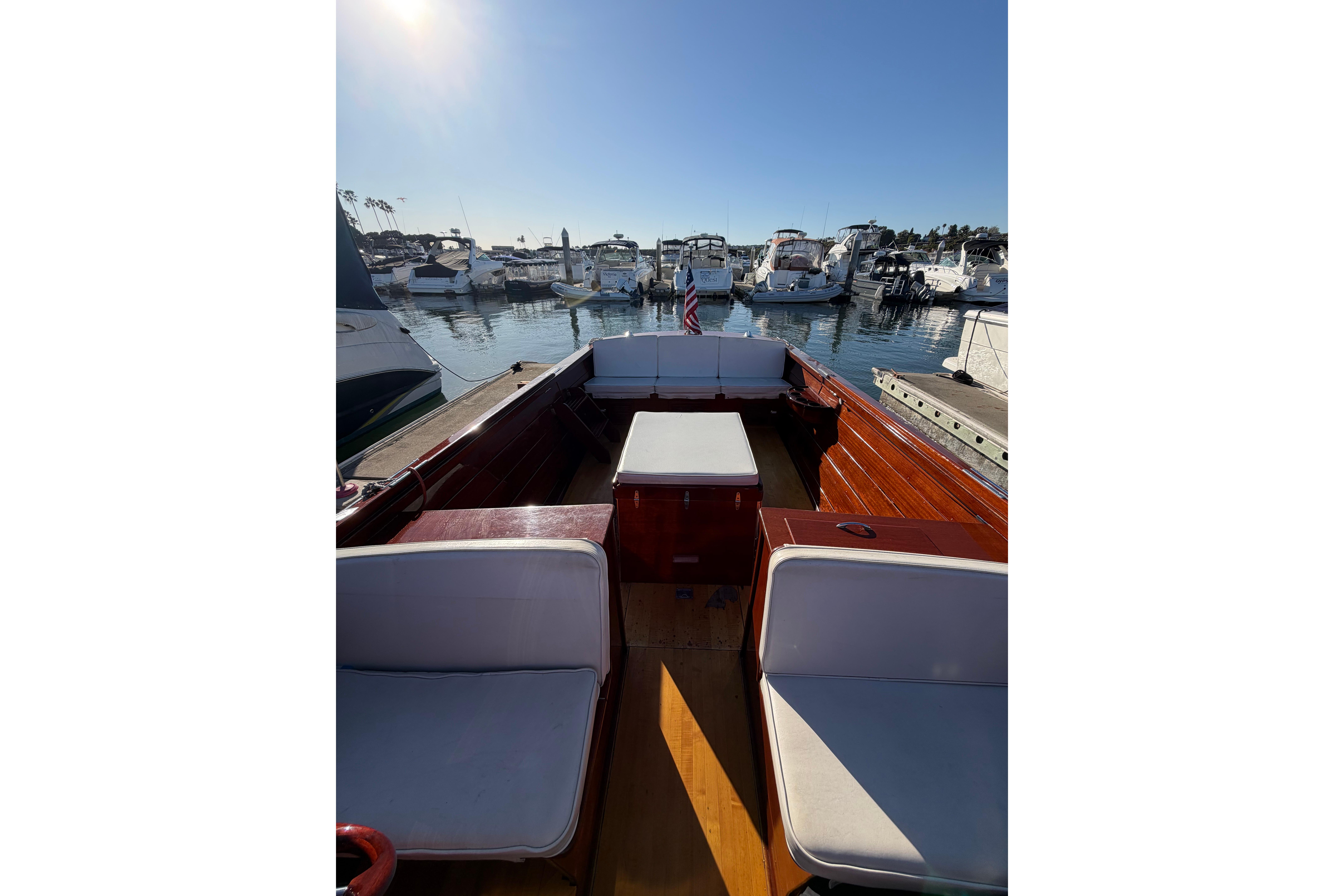 1964 Lyman 25 Sleeper boat interior with white seating, docked at a marina under clear skies.