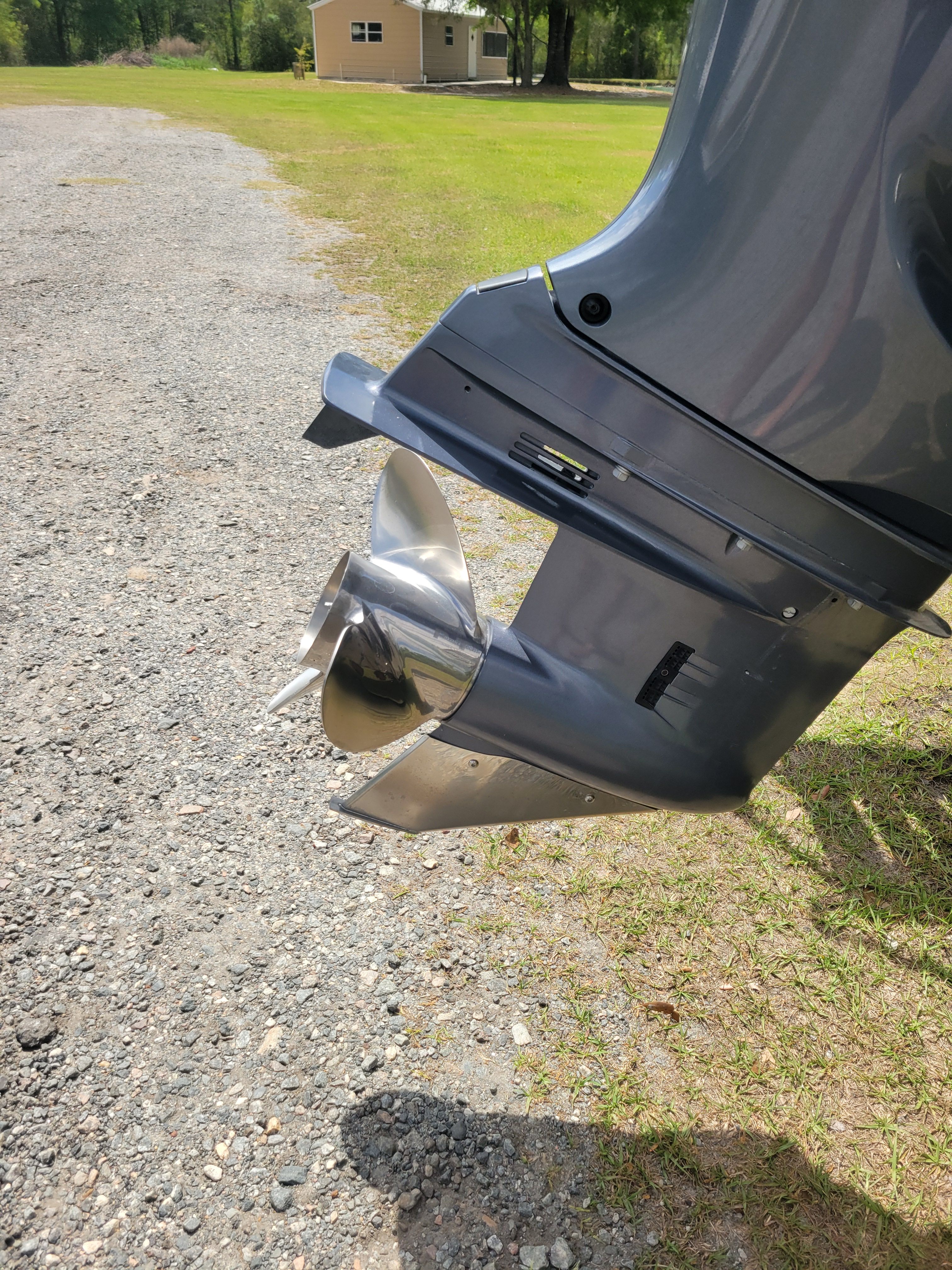A boat motor with a shiny propeller on a gravel path.
