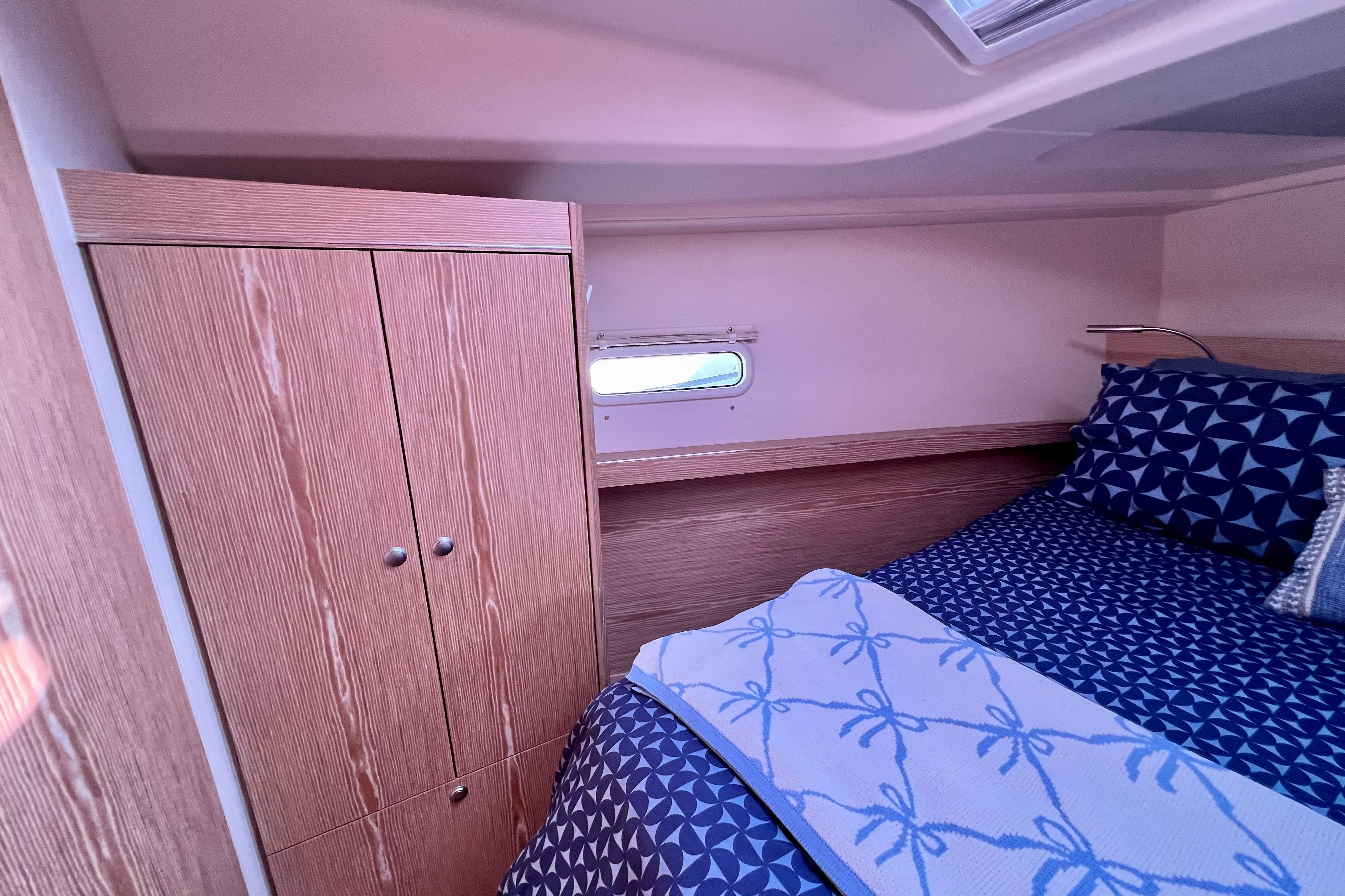 Cozy cabin interior of 2016 Hanse 455 yacht with wooden wardrobe and patterned bedding.