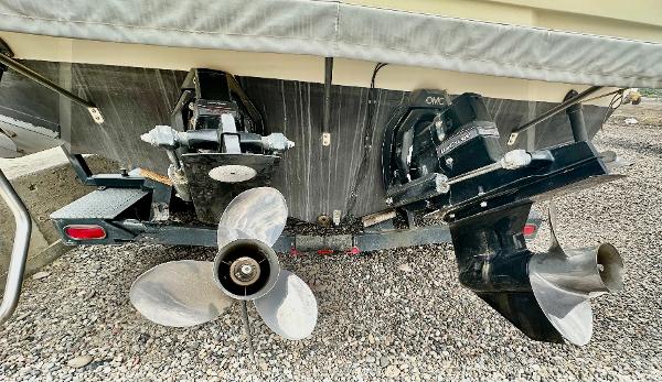 1987 Sea Ray 270 Sundancer boat stern with dual propellers and outdrives on gravel.