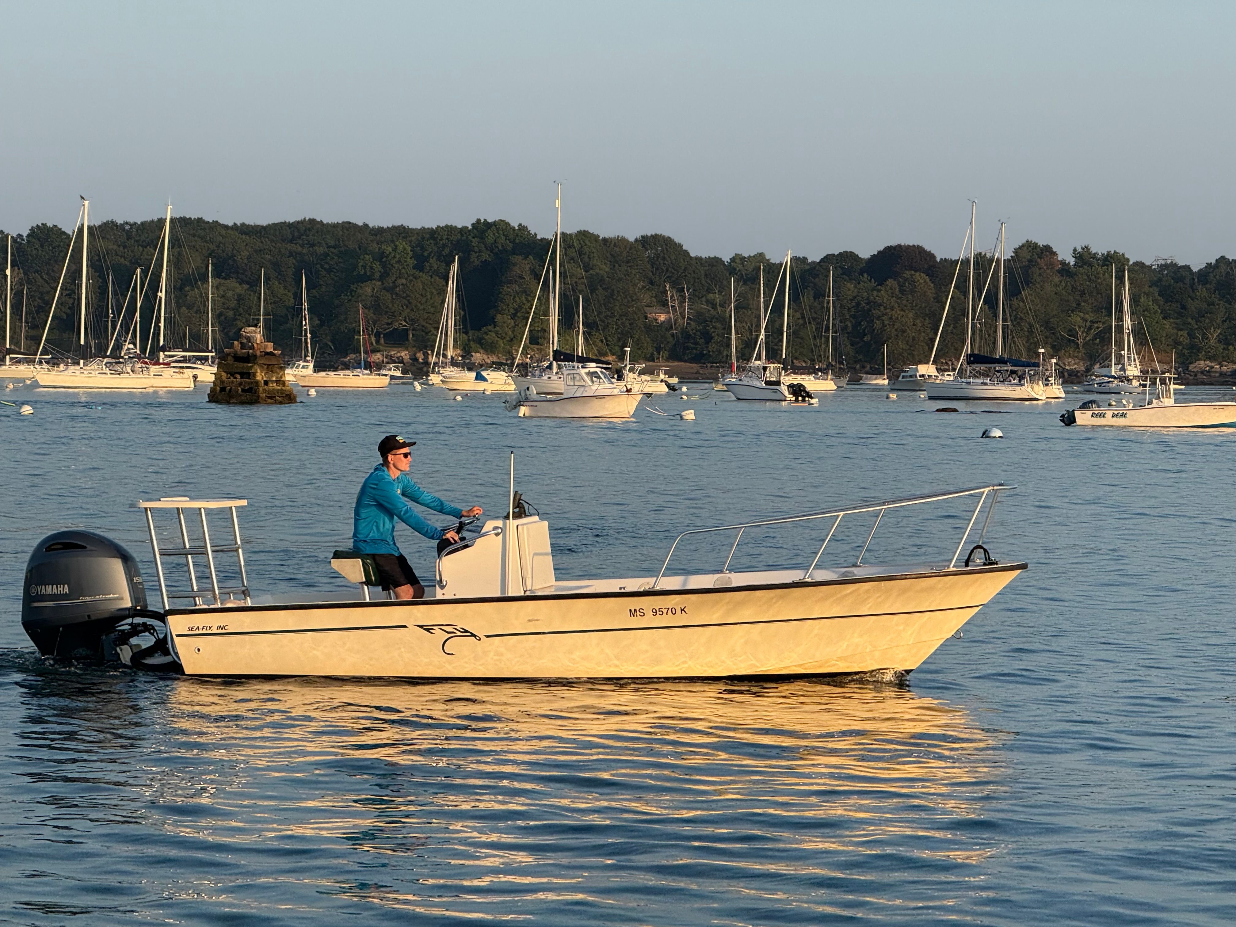 Man piloting 2004 Custom Sea Fly boat on calm water with sailboats in background.