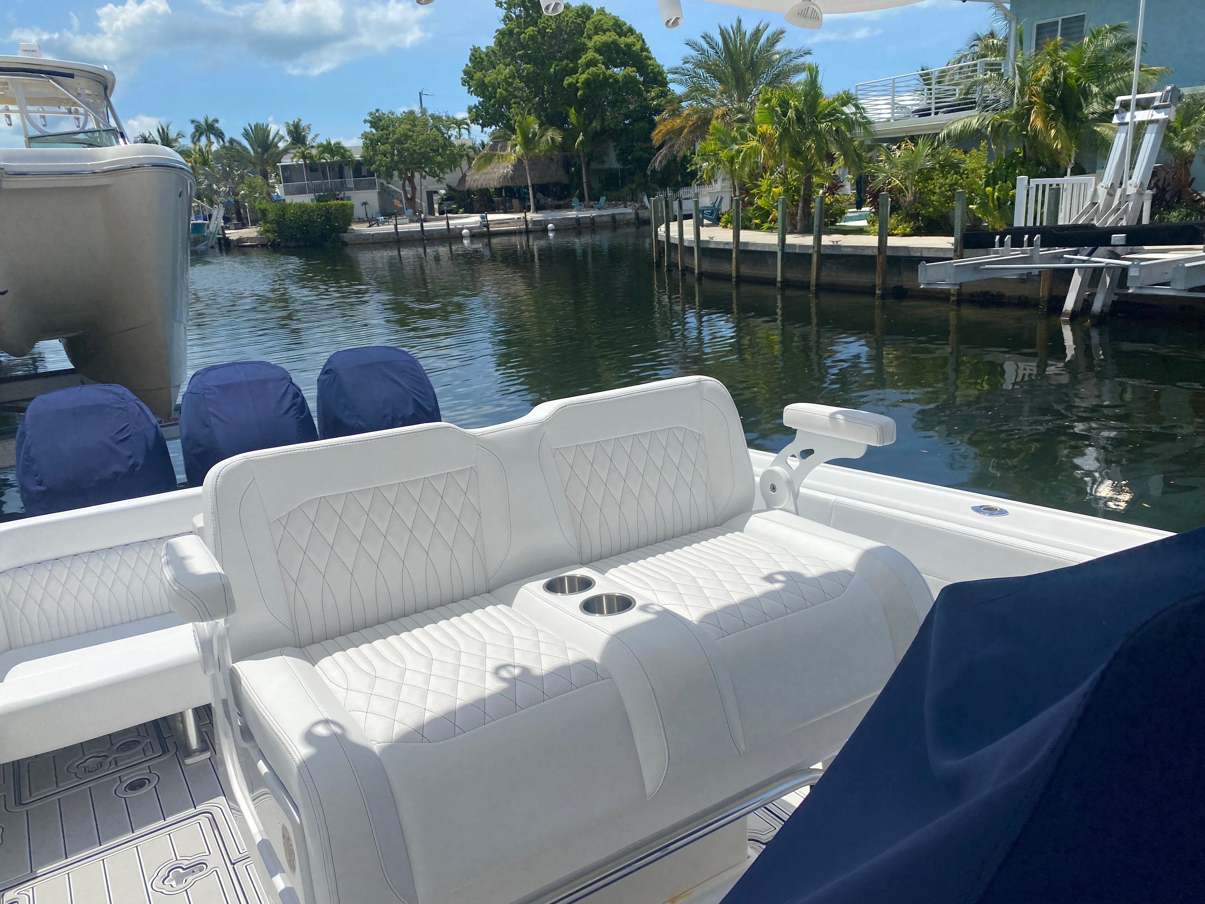 A sleek boat with white cushioned seats and cup holders, docked by a tranquil canal.