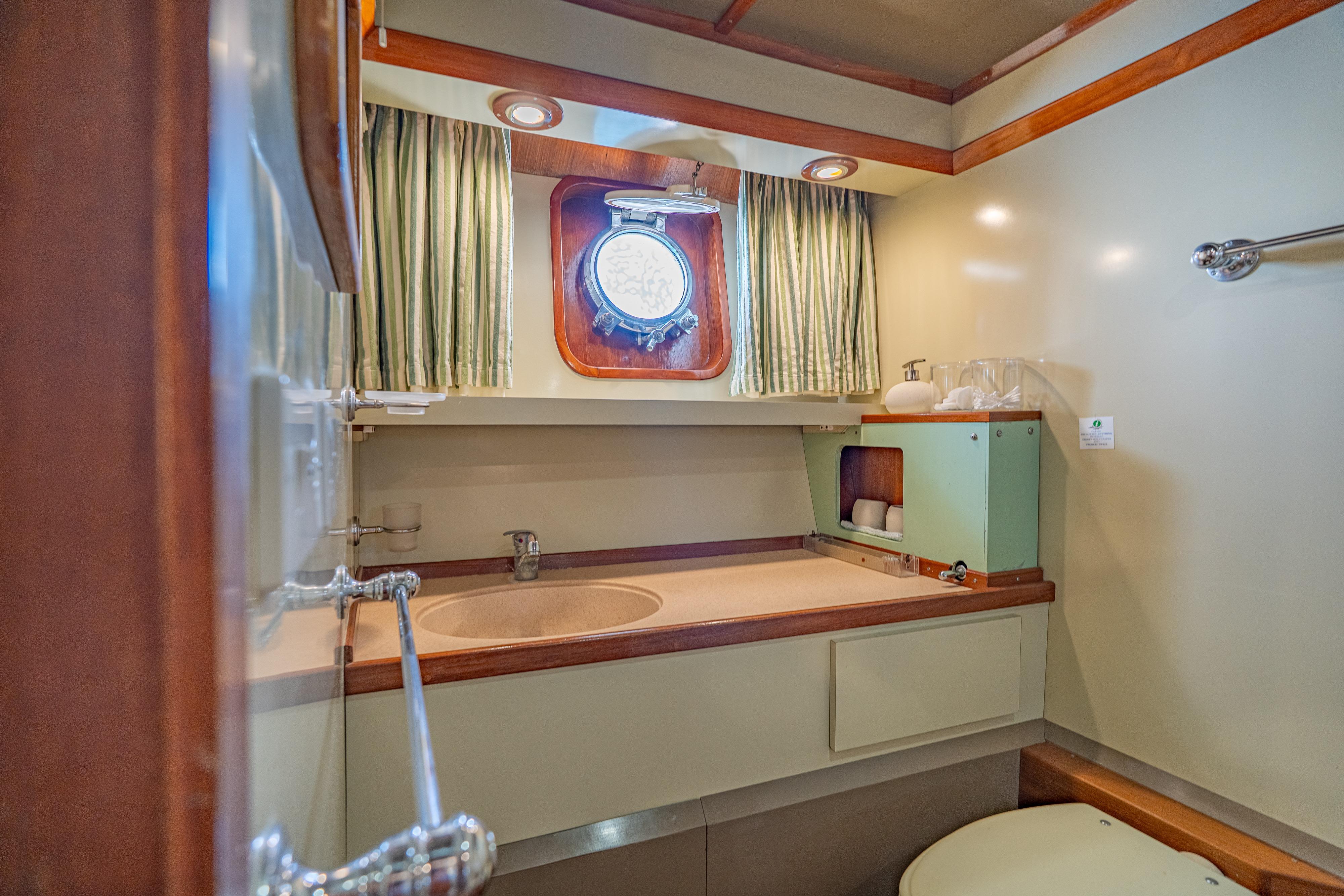 Vintage 1962 De Beer Round Stern 32 yacht bathroom with porthole and wooden accents.