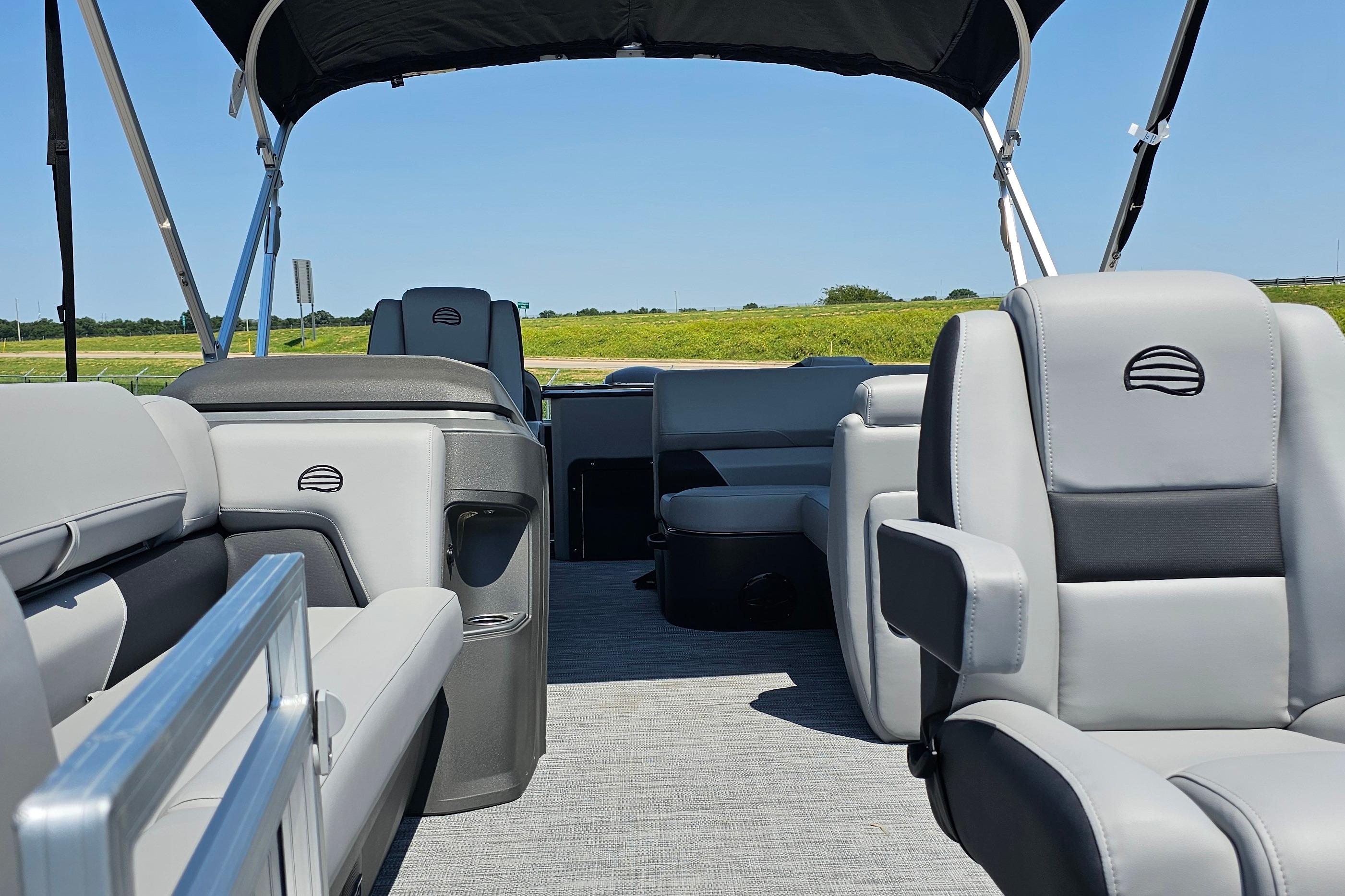 2026 Sun Tracker SportFish 20 DLX interior with gray seating and canopy, set against a sunny landscape.