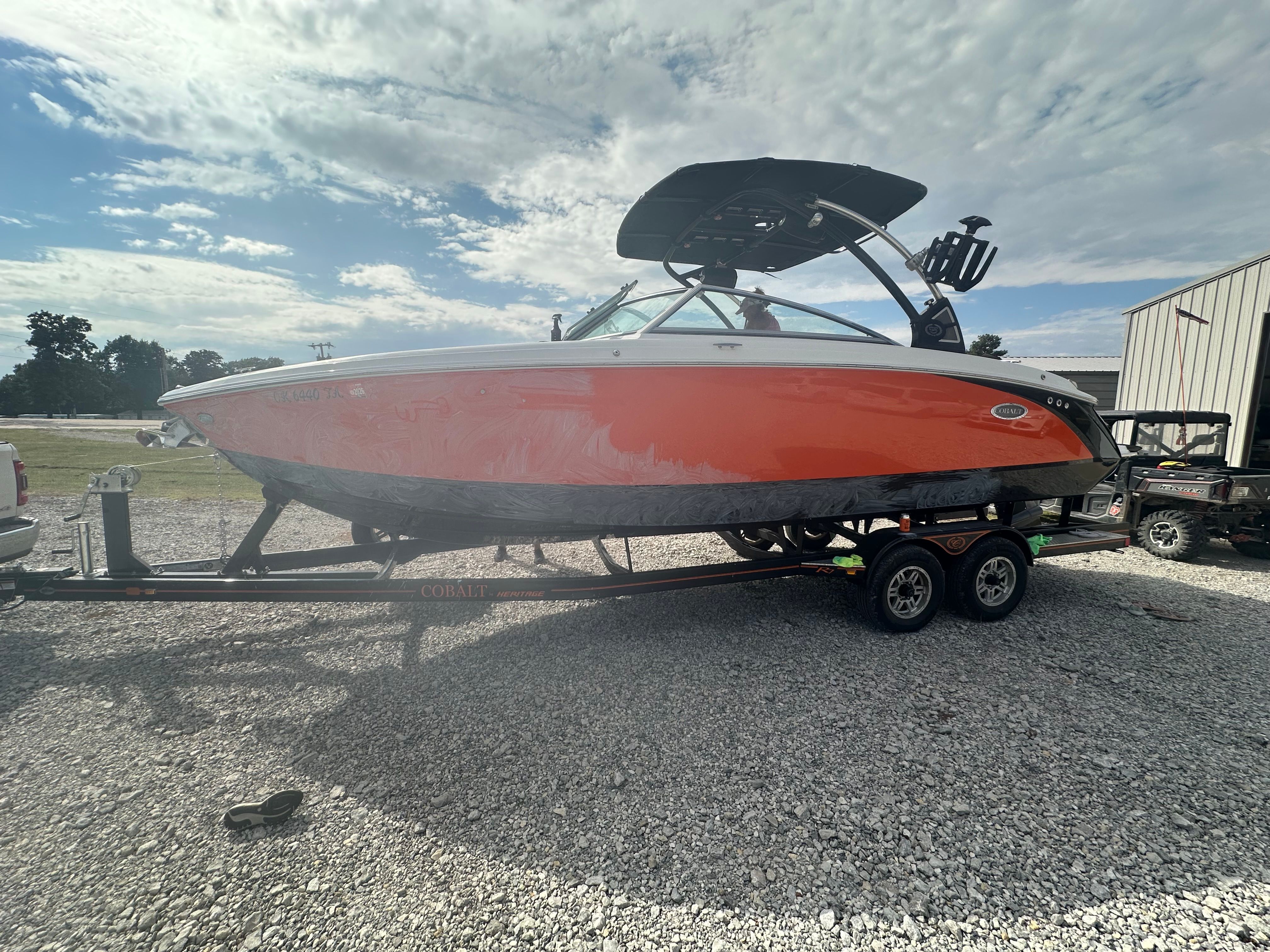 A 2019 Cobalt R7 Surf boat in orange sits on a trailer in a gravel lot.