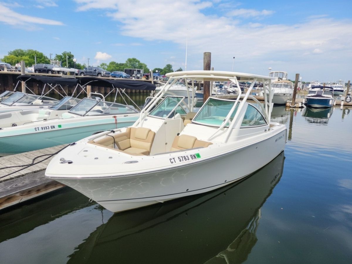 A white motorboat docked, featuring beige seating and a protective T-top.