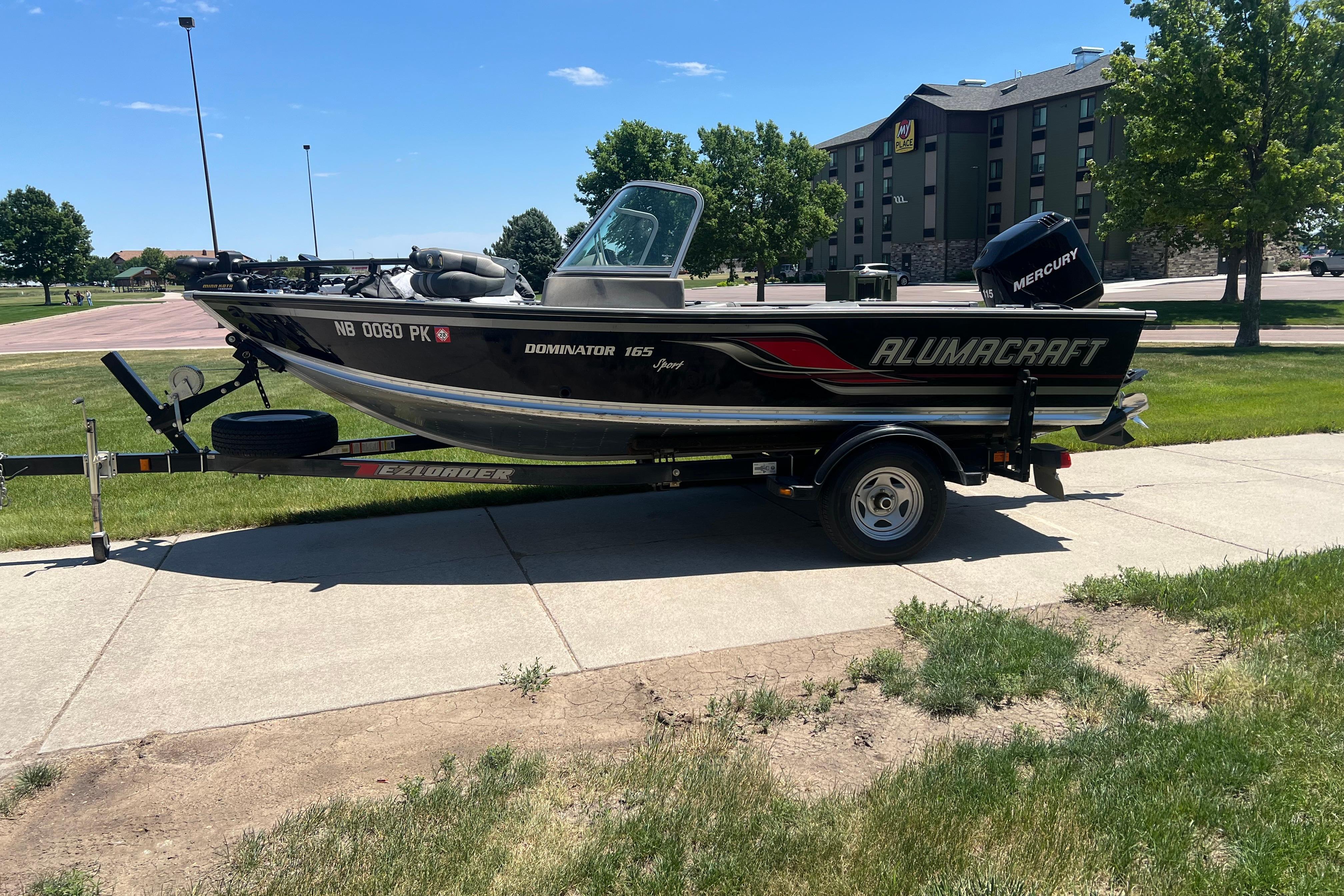 2010 Alumacraft Dominator 165 Sport boat on trailer, parked outdoors on a sunny day.