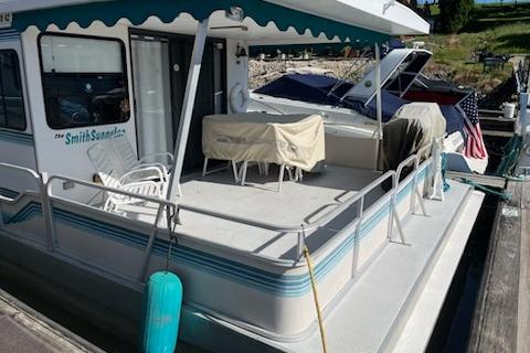 1994 PlayCraft 5215 houseboat docked with covered furniture and American flag.