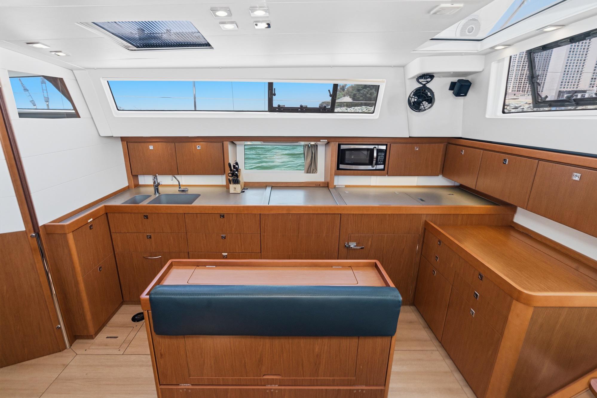 Interior of 2017 Beneteau Sense 50 yacht, featuring modern kitchen with wood cabinetry and large windows.