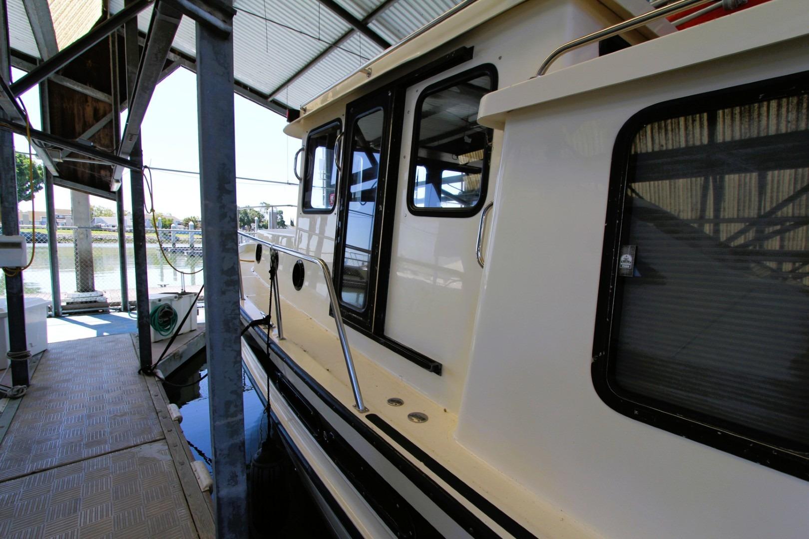 2002 Nordic Tug 37 docked under a covered marina, showcasing its side profile and windows.