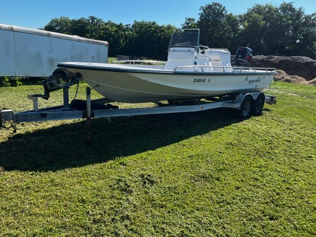 A white boat on a trailer is parked on grass.
